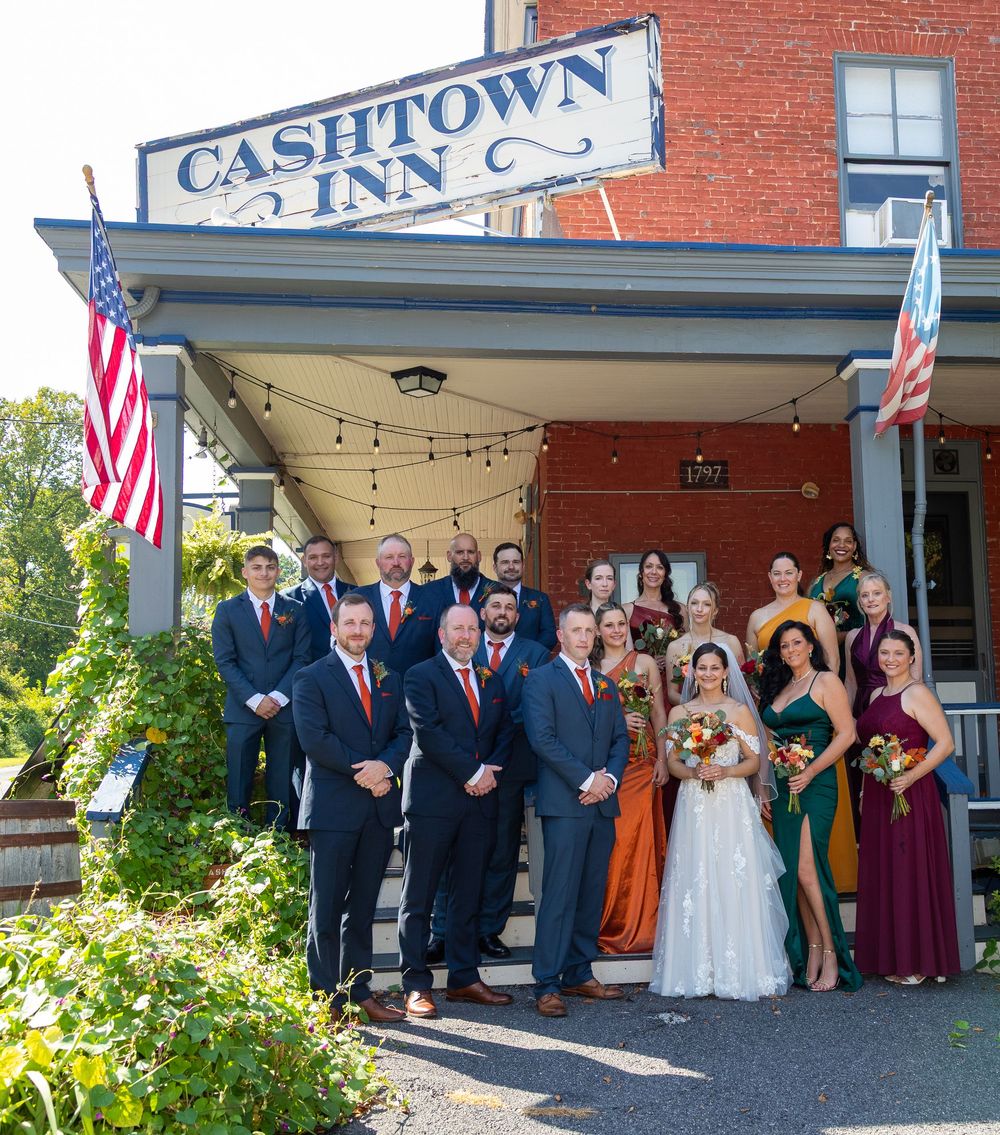 Wedding party poses on steps of historic Cashtown Inn, bride in white gown with groomsmen and bridesmaids in fall colors.
