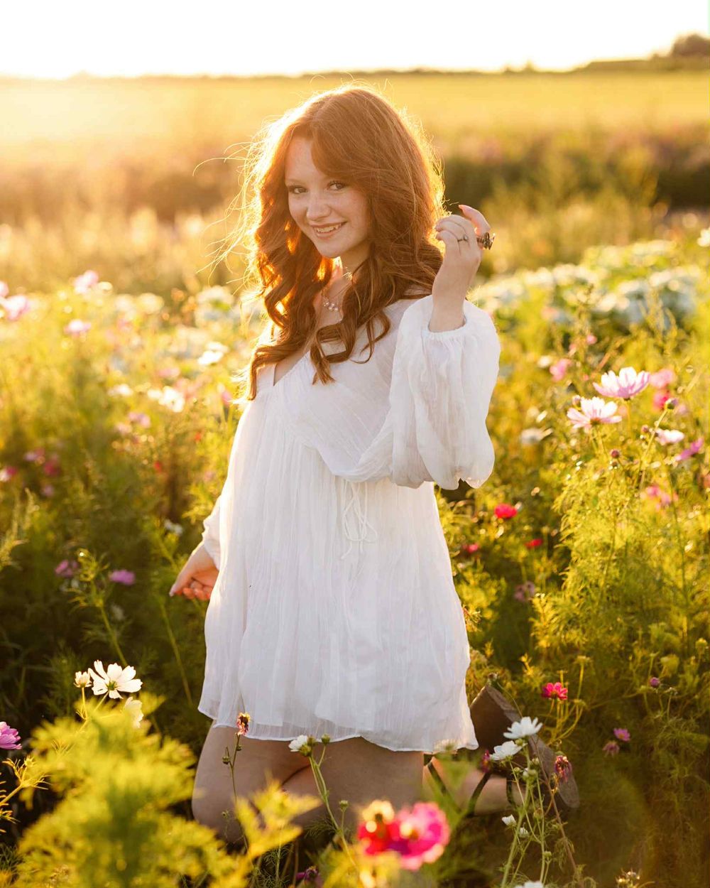 Senior Portraits in a white dress stands among vibrant wildflowers during golden hour sunset in a meadow in Petoskey Michigan