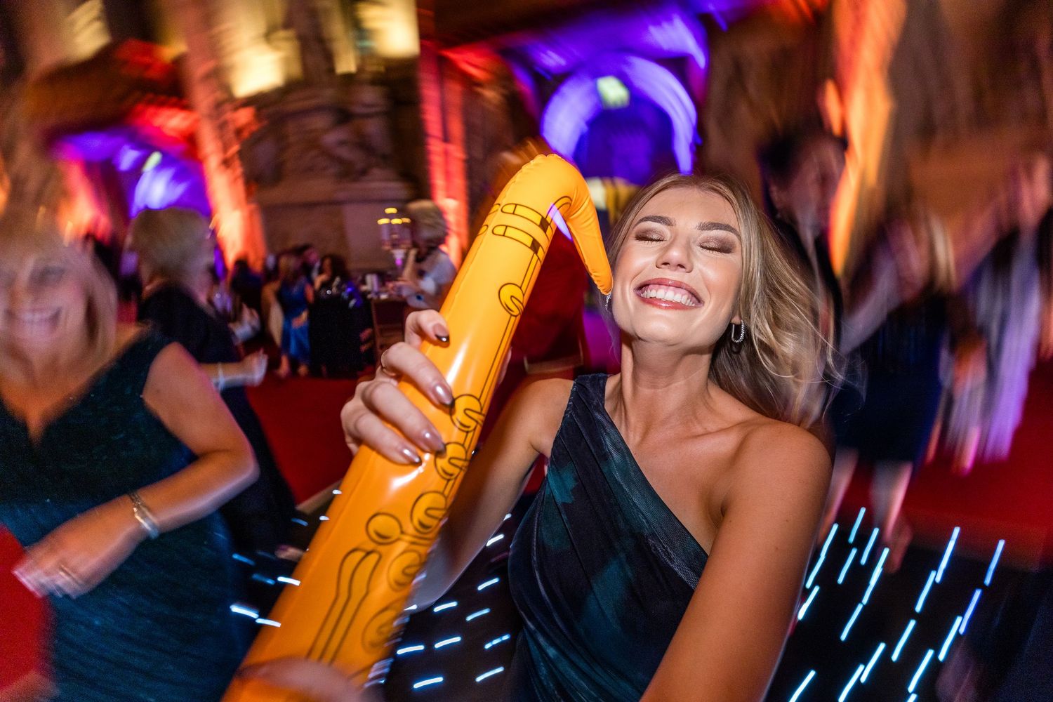 People dancing and celebrating at a nightclub with colorful lighting and bottles of champagne.