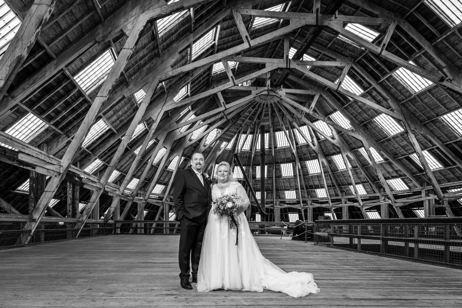 A black and white wedding photo sequence showing a couple walking through a grand architectural space with exposed beams.