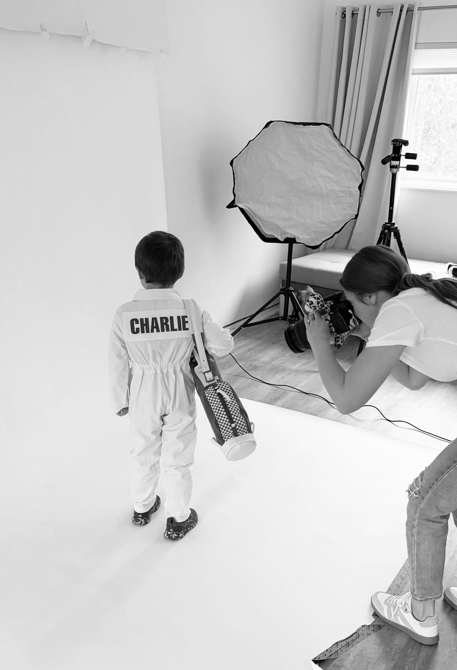 Behind-the-scenes photo shoot setup showing person in white outfit on seamless white background in photography studio.