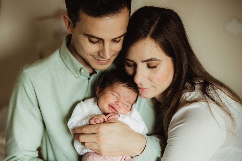 Happy young parents holding their sleeping newborn baby together in a warm, intimate family portrait.