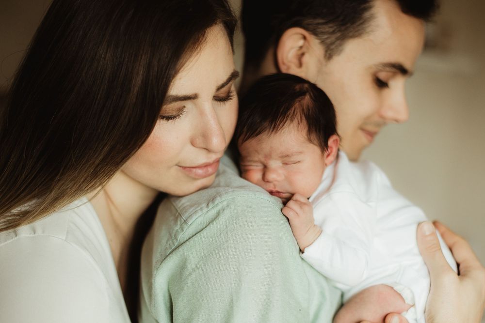 Happy parents holding their sleeping newborn baby wrapped in a soft green blanket.