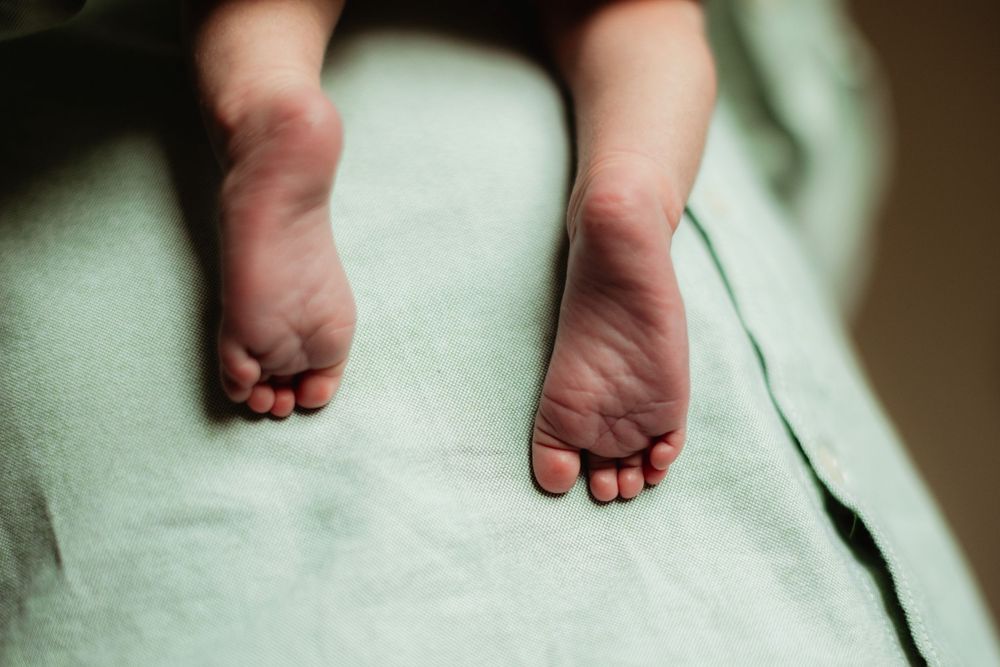 Close-up of tiny newborn baby feet resting on a soft mint green blanket.