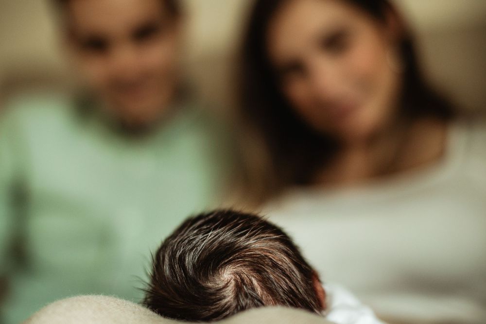 Close-up of a newborn baby's head with two blurred parents smiling in the background.