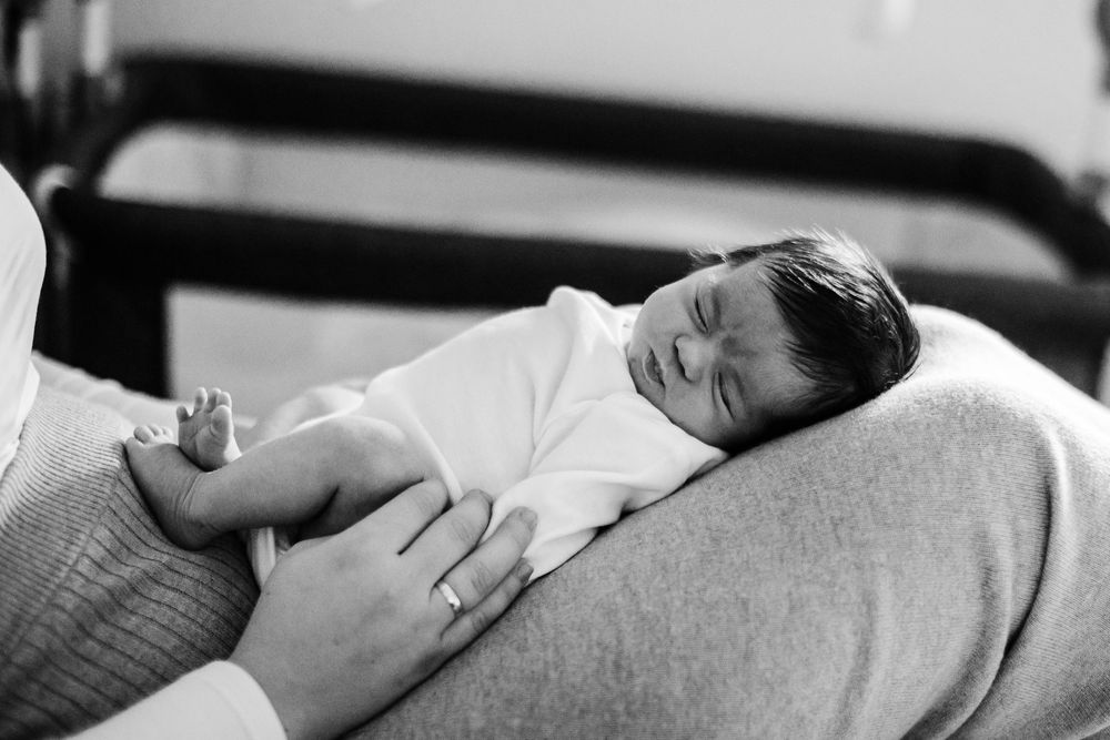 Black and white photo of a sleeping newborn baby cradled in an adult's arms on a soft cushion.