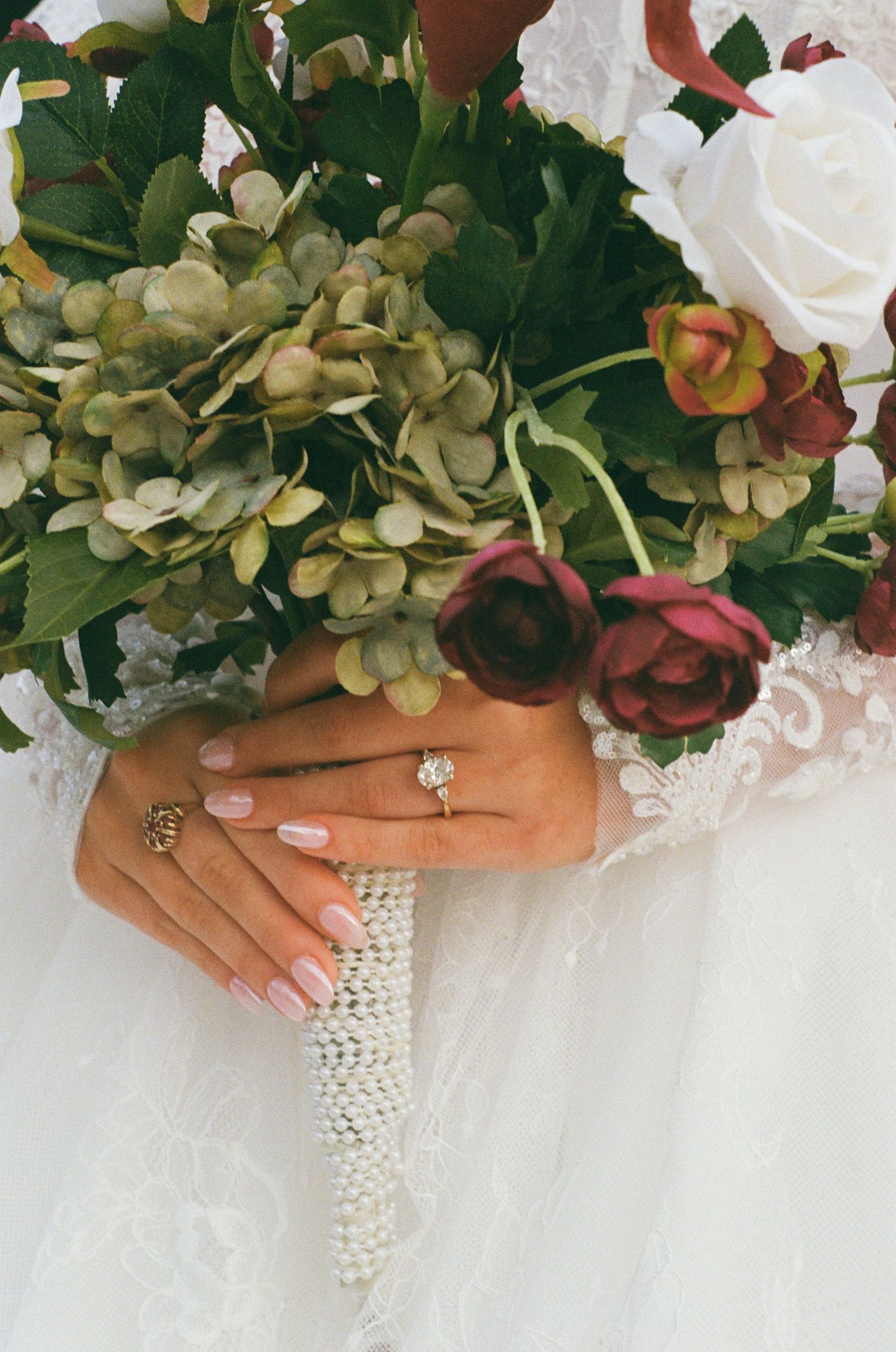 Bride holding a bouquet of roses and hydrangeas, showcasing a diamond engagement ring and pink manicure.