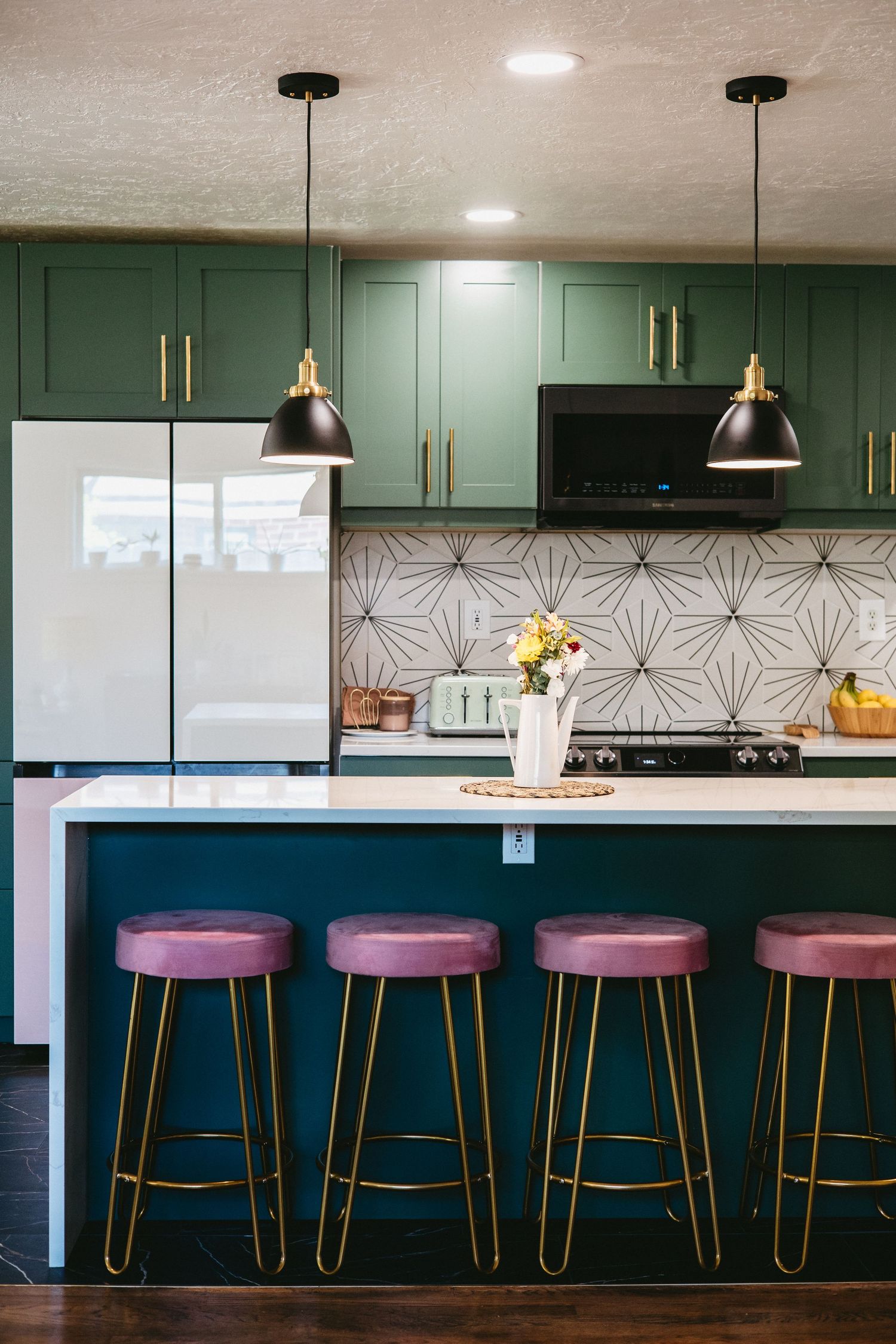 a retro inspired kitchen with green cabinets, gold finishes, pink hair pin barstools, white and black tiles, and clean white countertops