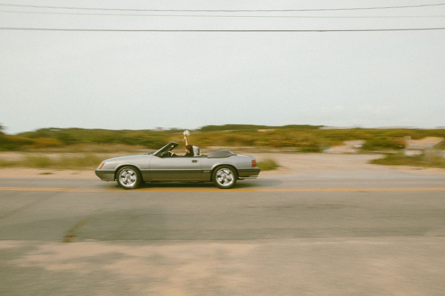 A convertible car drives past on a coastal road in motion blur.