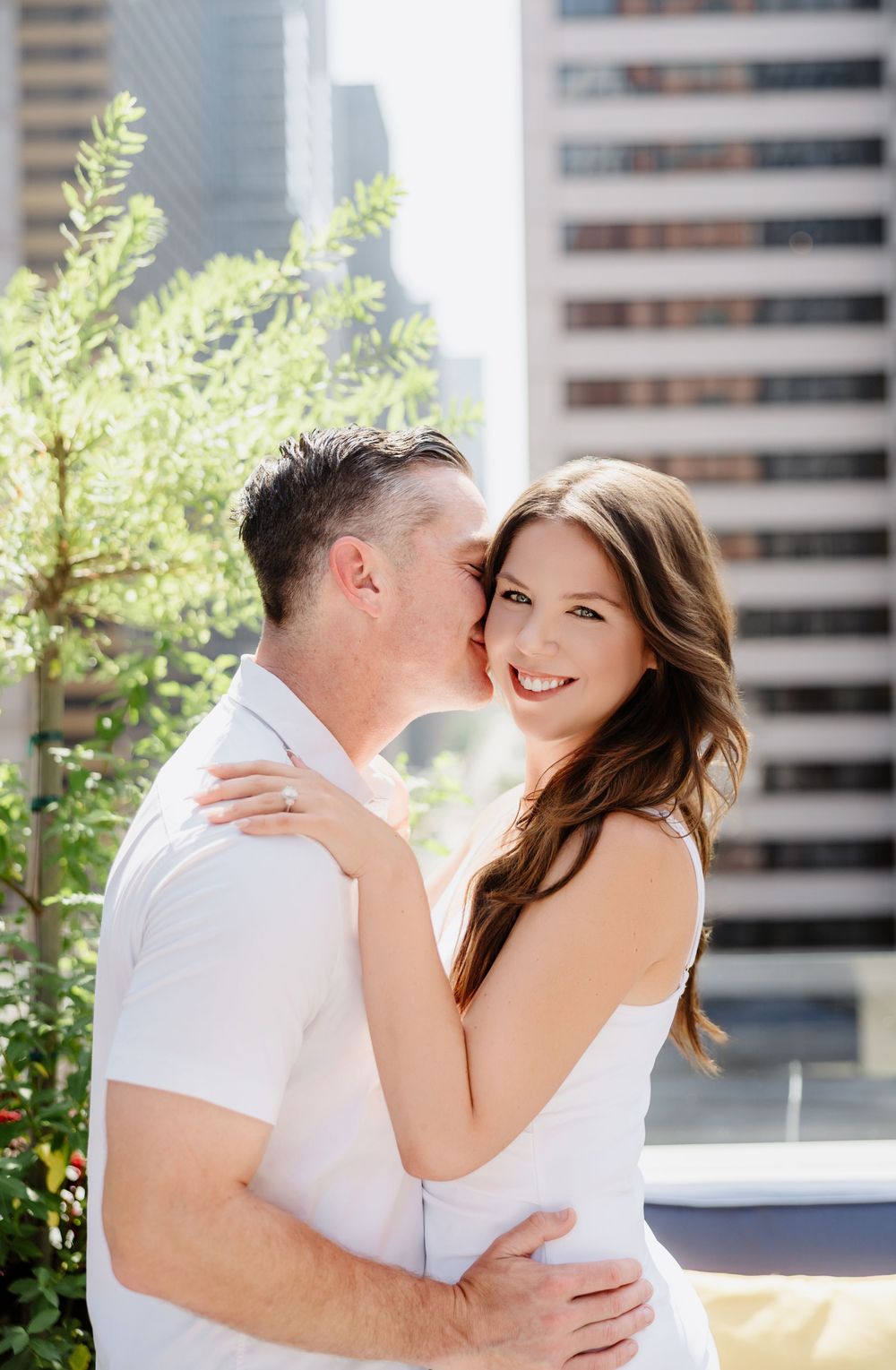 A romantic urban couple embraces while sharing an intimate moment against a cityscape backdrop.