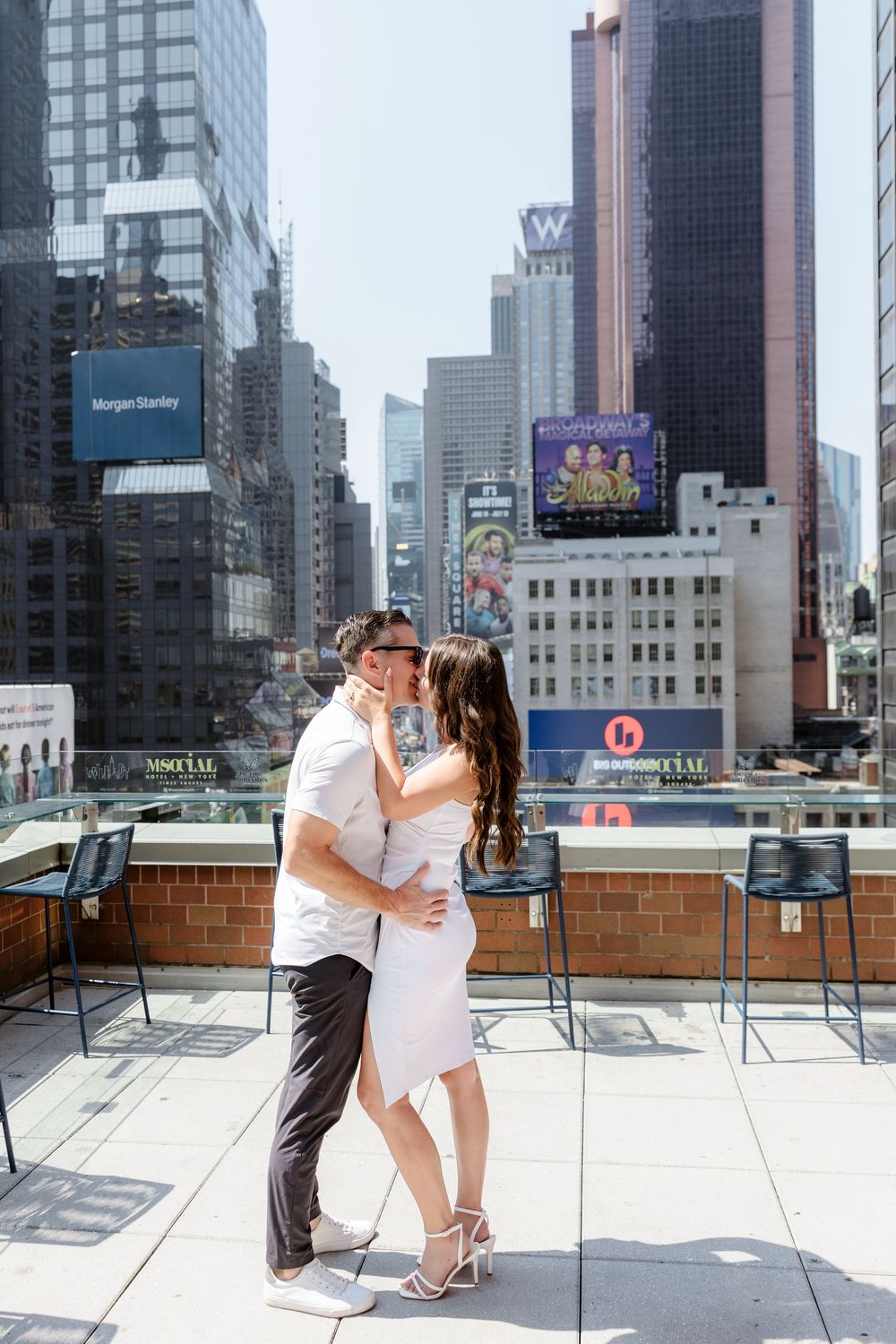 A couple shares a romantic moment on a rooftop terrace overlooking urban skyscrapers in New York City.