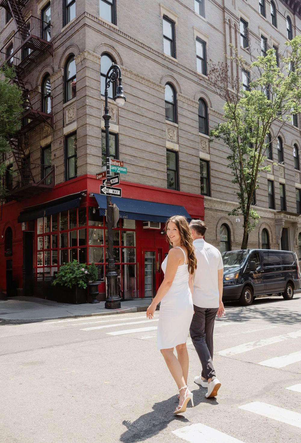 A couple walks hand in hand down a sunny city street with classic brick buildings.