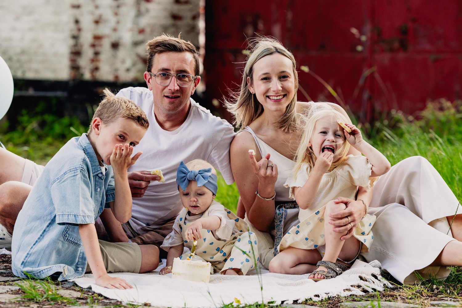 An extended family enjoys a relaxed picnic gathering on a blanket in an outdoor setting.