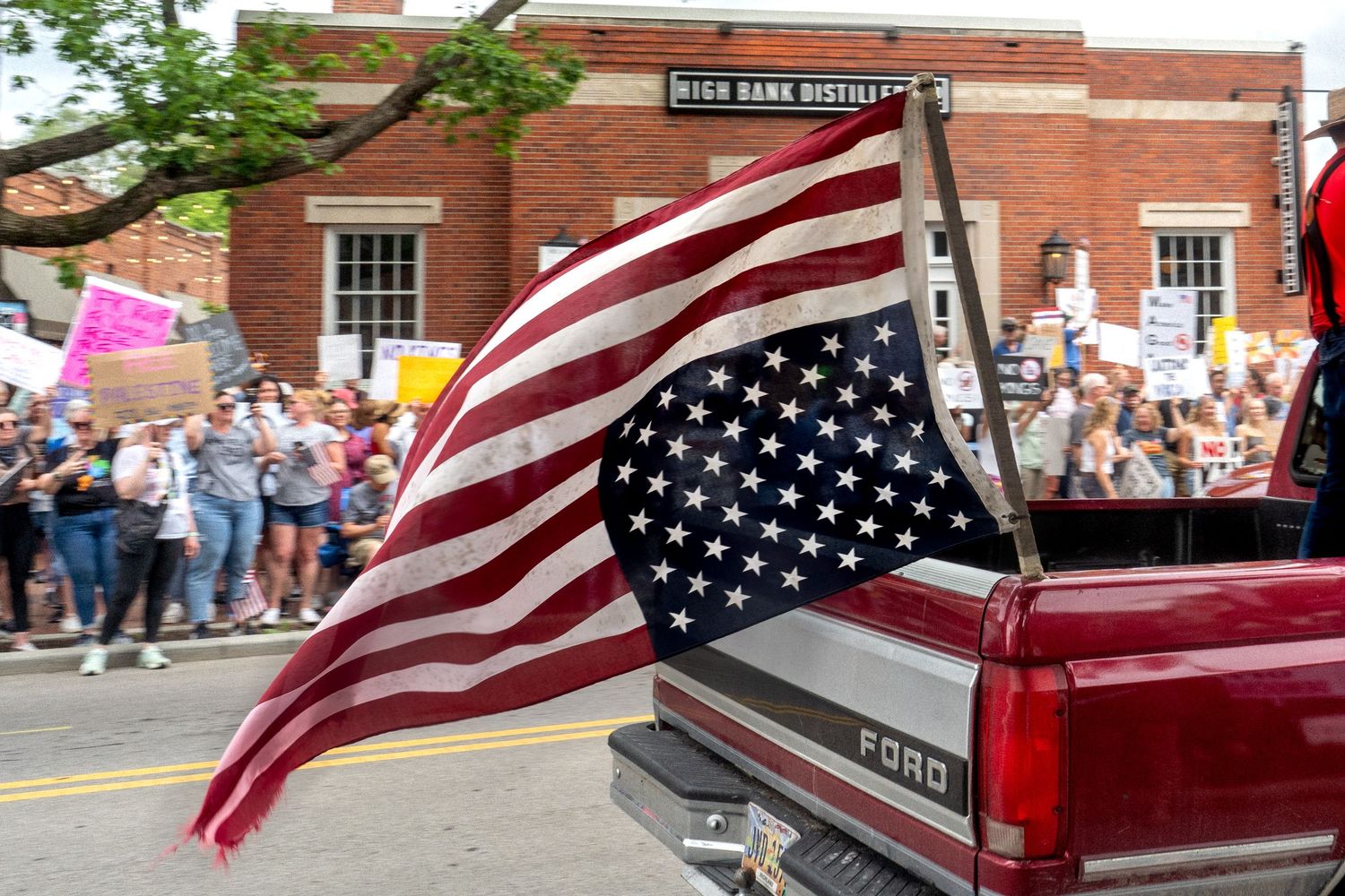 American flags wave alongside a parade of classic red cars during a small town celebration.
