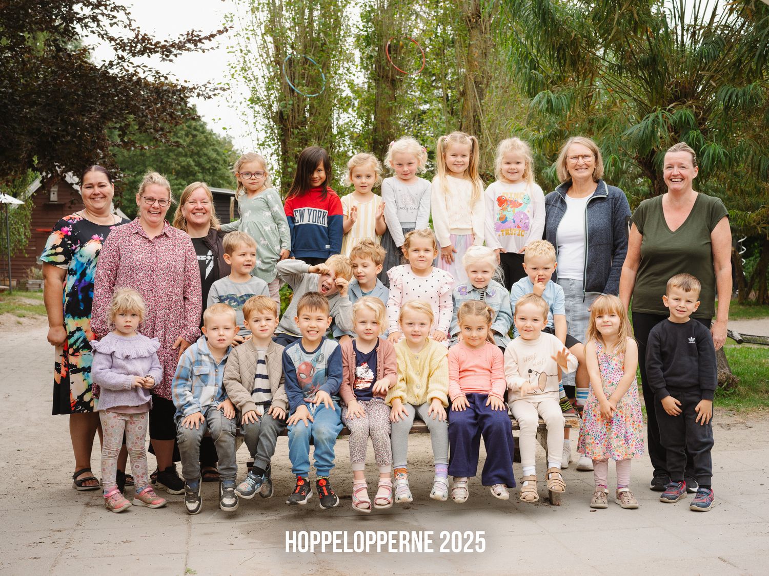 Large group of young children sitting together for a preschool photo session in a garden setting.