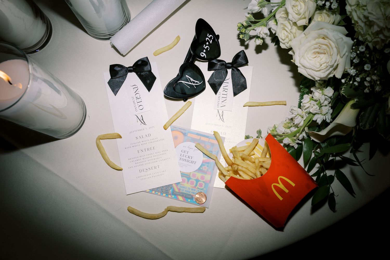 Wedding invitation suite with white roses, candles, and ribbons arranged on a light background.