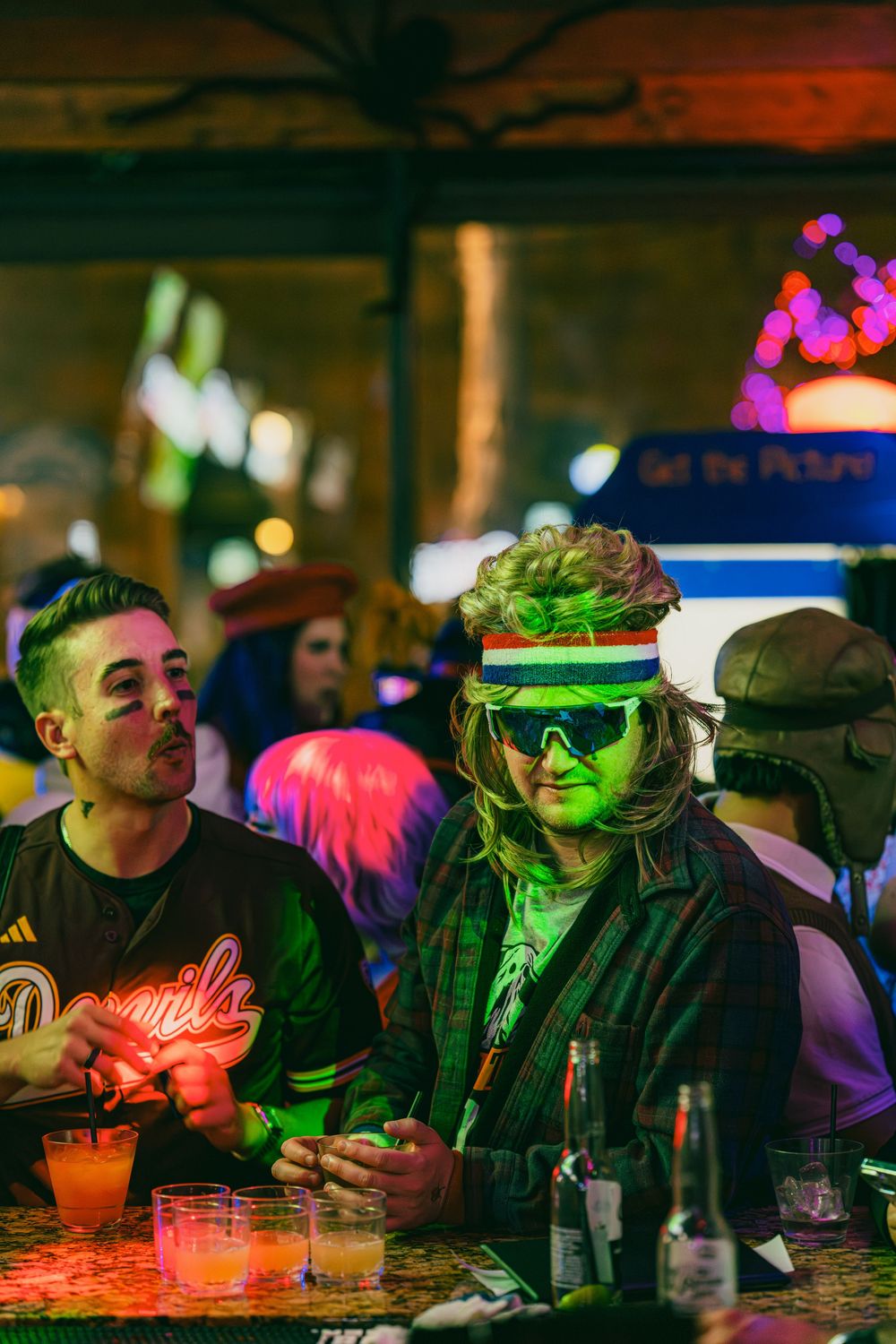 People sitting at a dimly lit bar with vibrant red and green lighting creating a moody nightlife atmosphere.