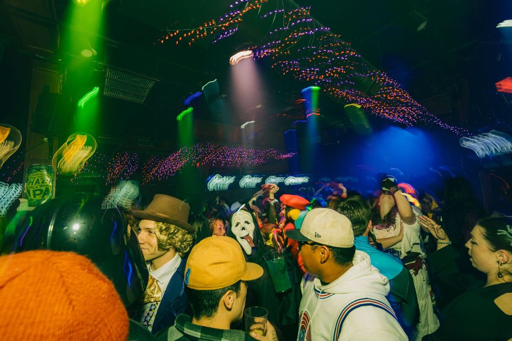 Crowded nightclub scene with colorful lights and string decorations overhead as people gather on the dance floor.