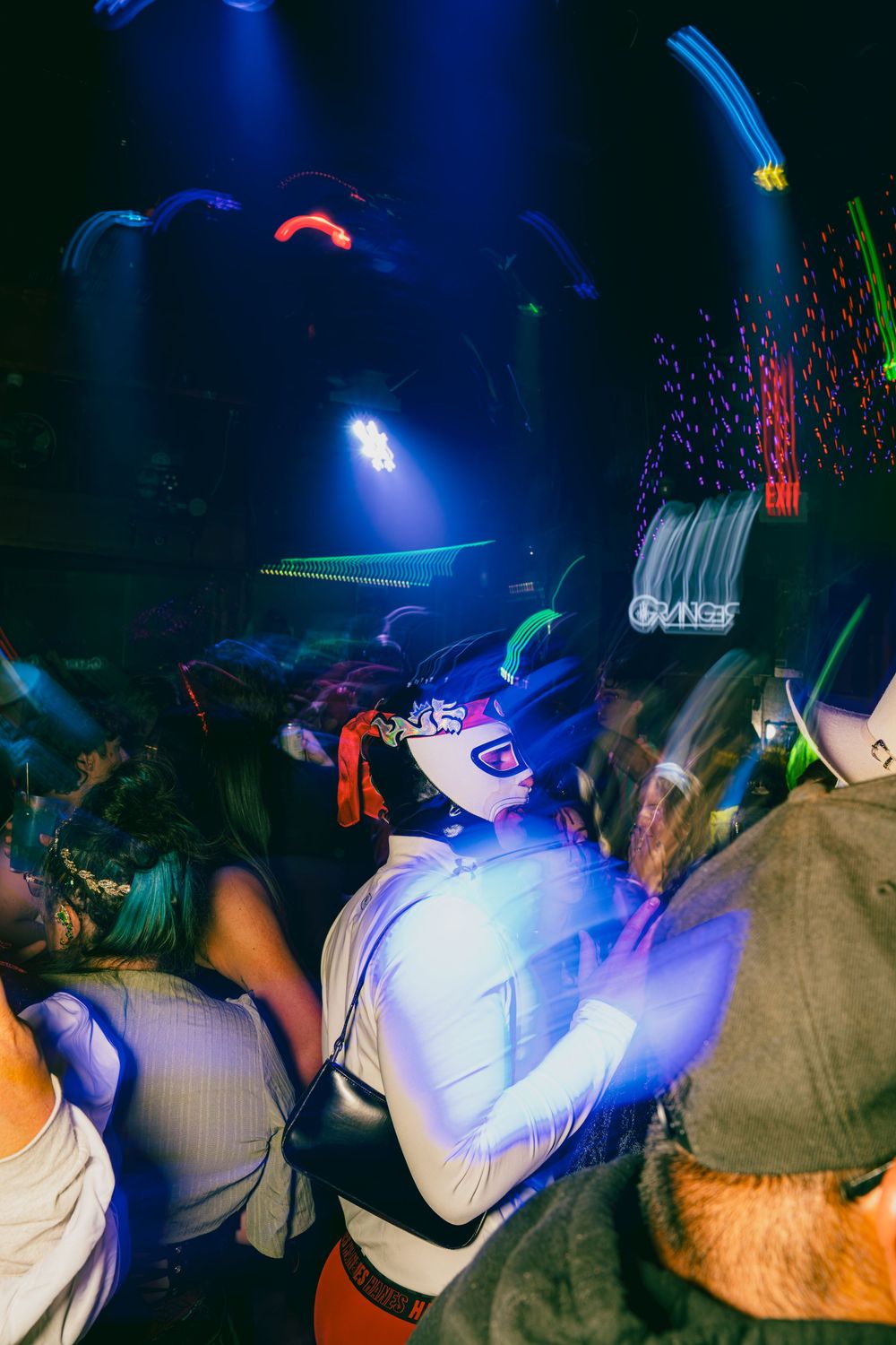 People dance at a nightclub under blue lighting while wearing white shirts and baseball caps.