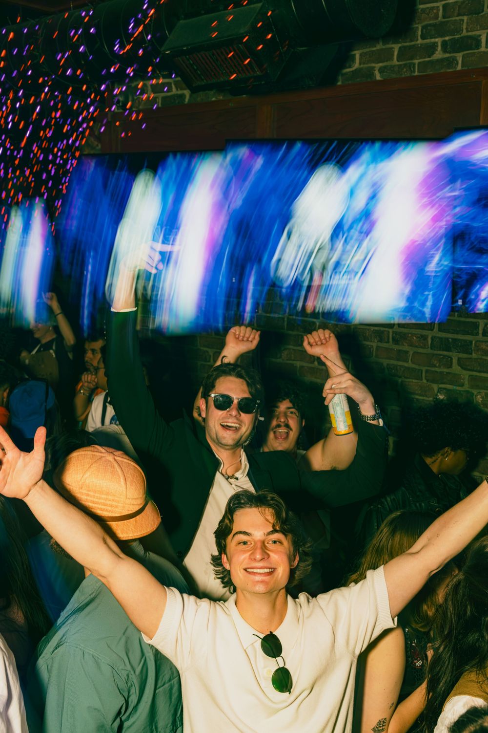 A lively nightclub scene with people dancing and raising their arms under vibrant blue lighting effects.