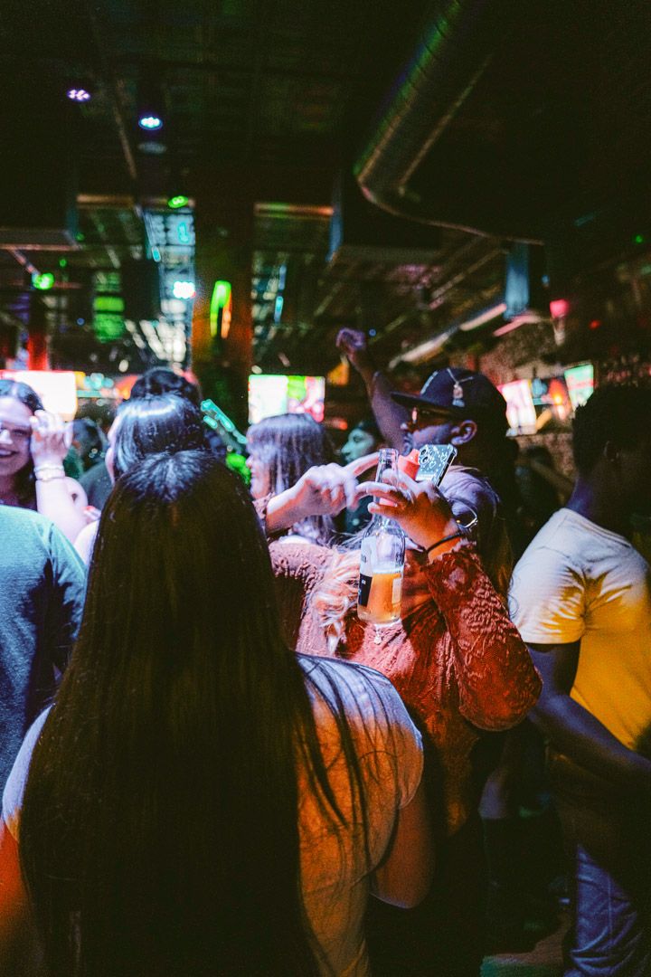 A crowded concert venue with people silhouetted against colorful stage lighting and LED screens in the background.