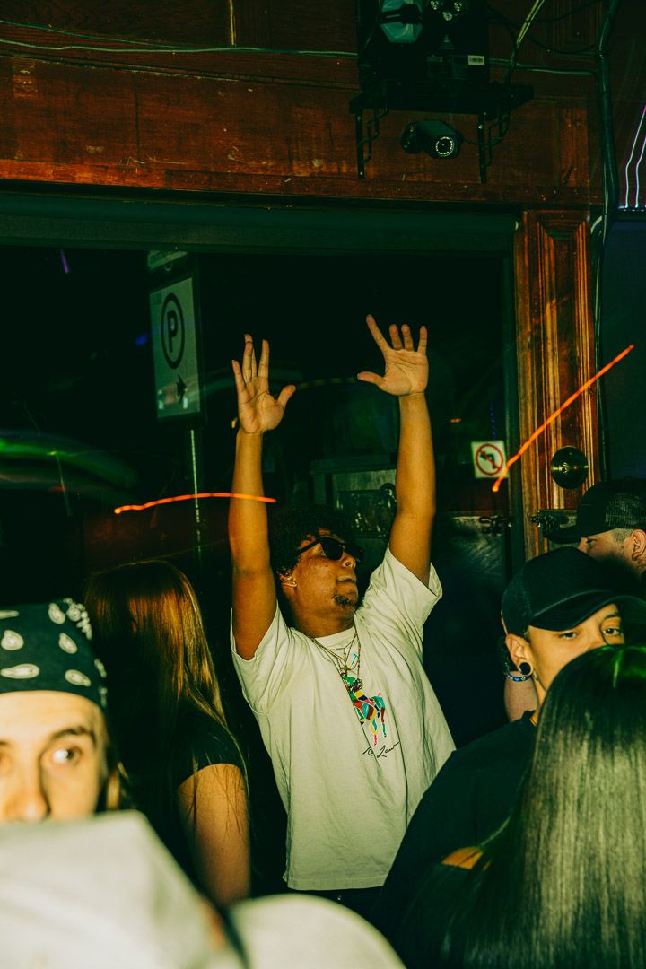 Energetic crowd member raises hands in excitement at nightclub with dark atmospheric lighting.