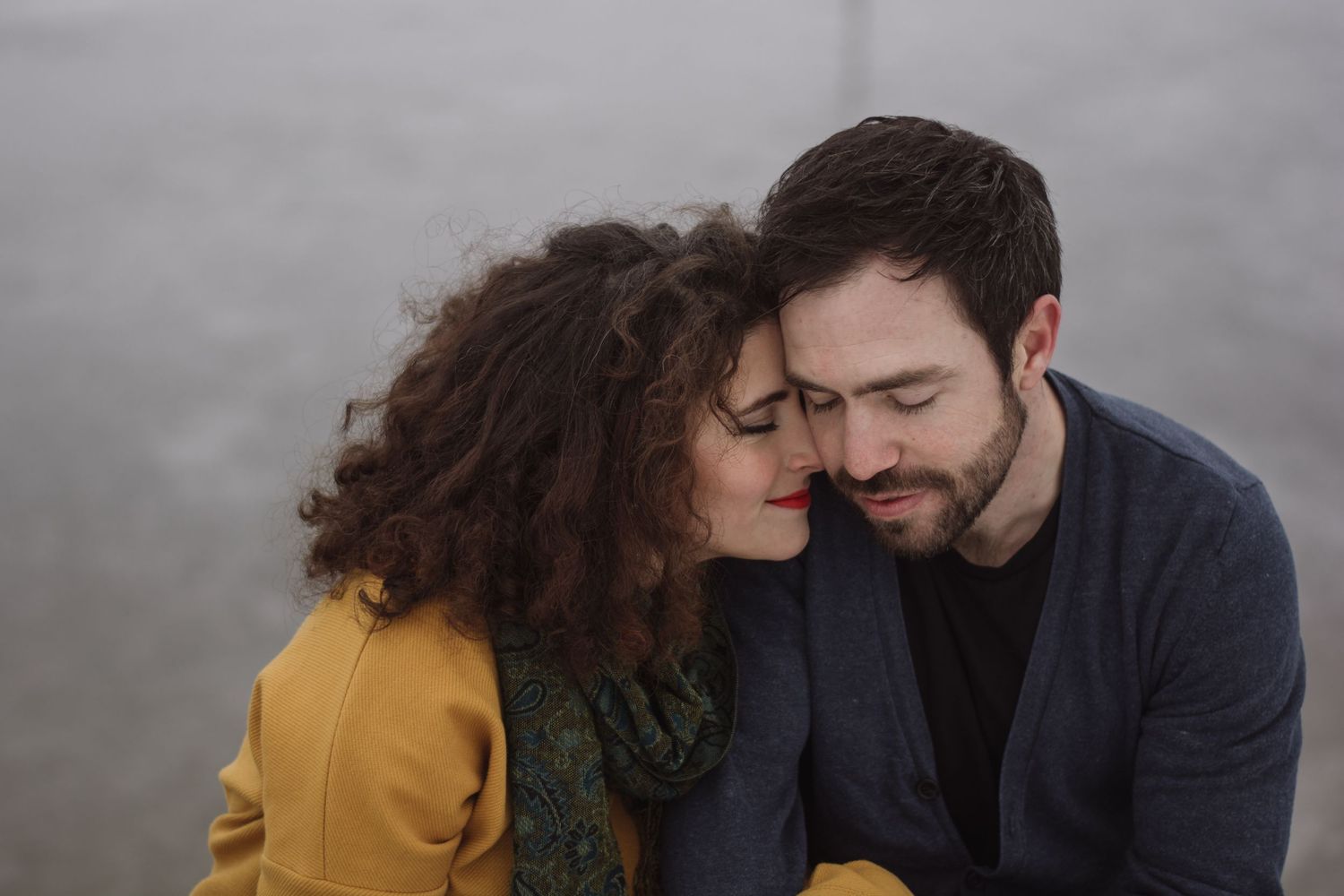 Romantic couple in yellow and navy blue outfits embracing in intimate poses against blurry backgrounds.