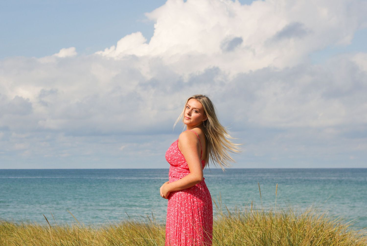 Pink maxi dress silhouette against ocean horizon and cloudy summer sky.