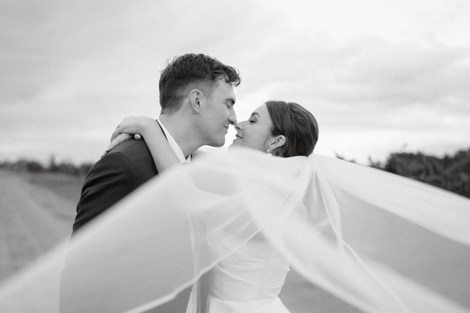 A romantic black and white portrait of a bride and groom sharing an intimate moment in a softly lit hallway.
