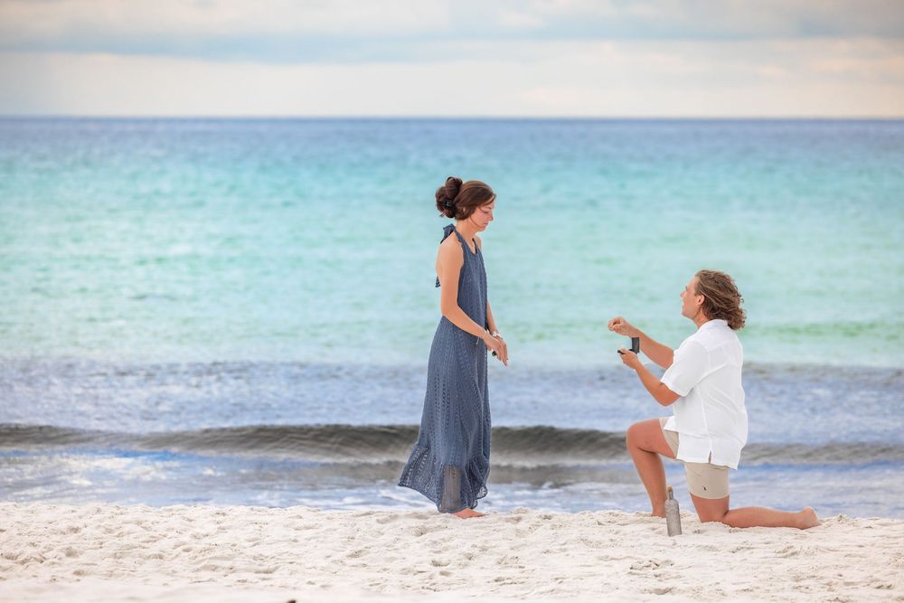 Romantic beach proposal scene at sunset with couple silhouetted against turquoise ocean waters.