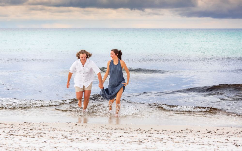 People walking and splashing along a scenic tropical beach shoreline at sunset with gentle waves rolling in.