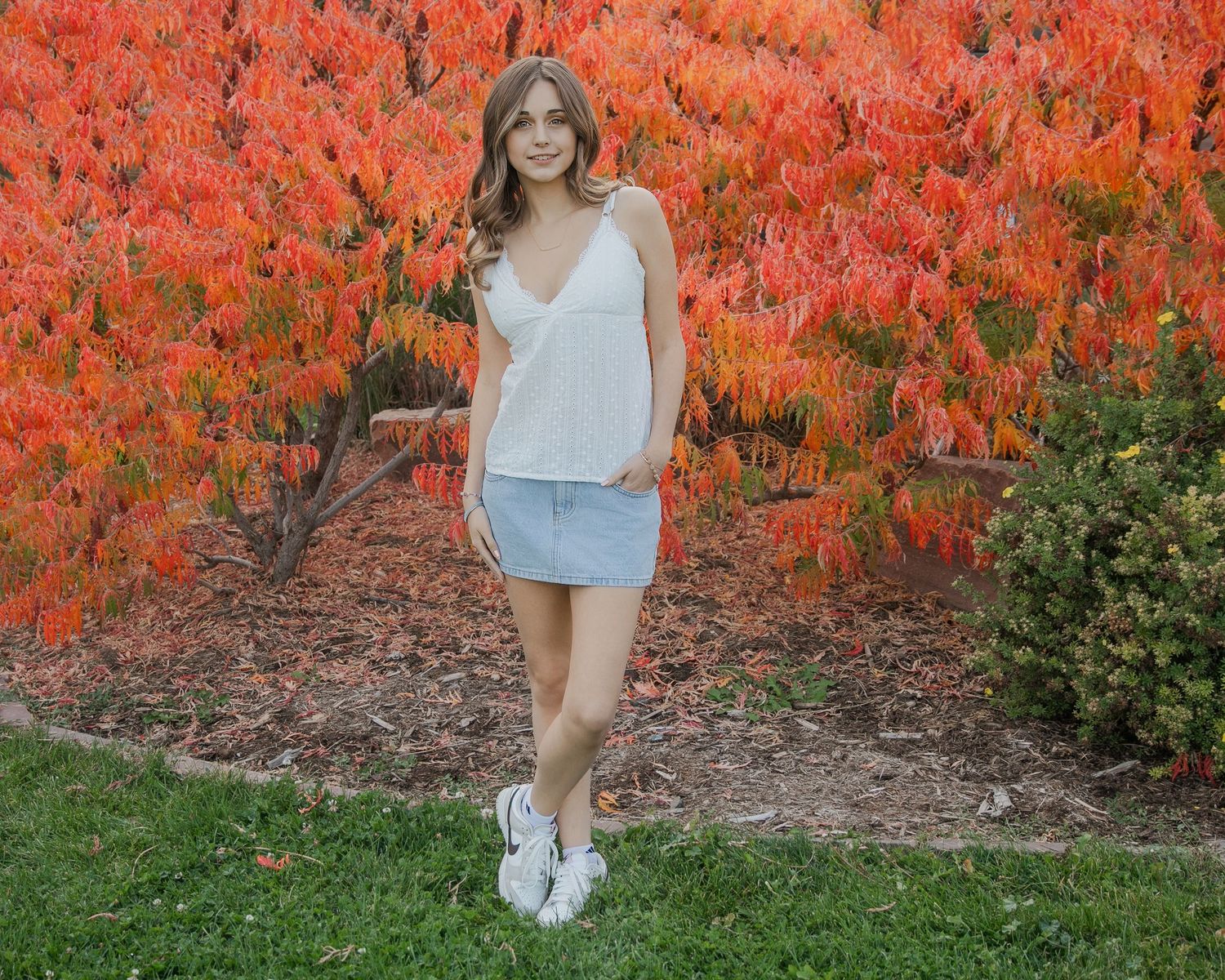 High school posing in front of fall foilage for her senior portraits.