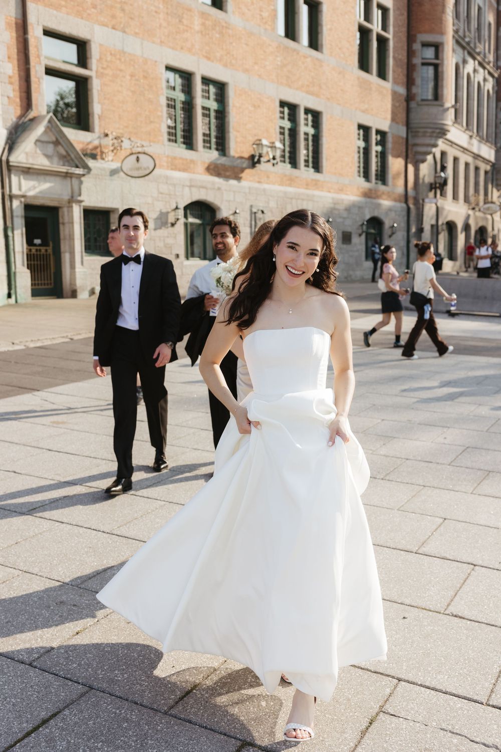A bride in a flowing white dress twirls and dances joyfully on a bright stone plaza.