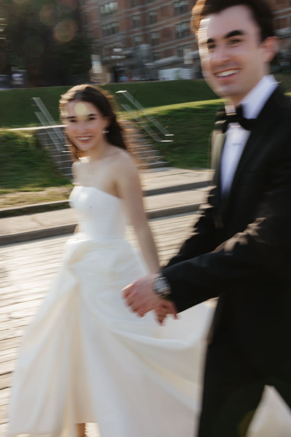 A couple joyfully walks together on their wedding day, with the bride in a strapless white gown and groom in a tuxedo.