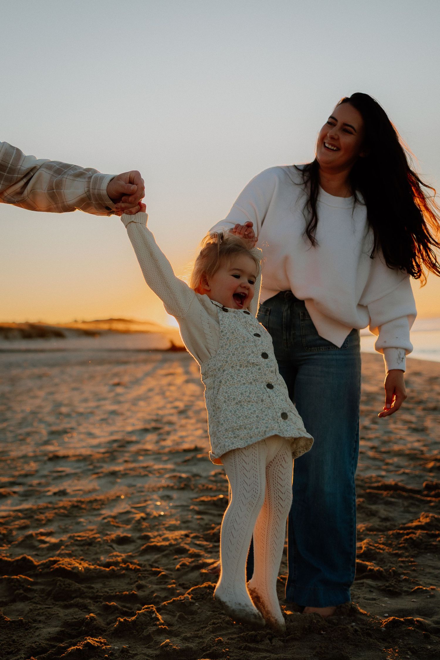 A parent and child playing joyfully together on a beach at sunset during a golden hour photoshoot.