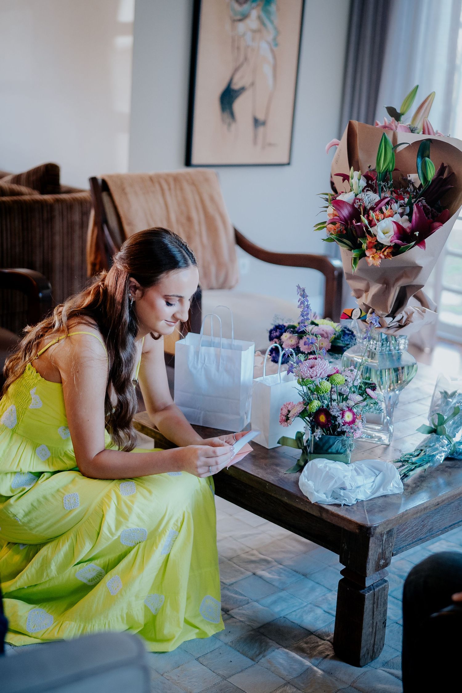Someone wearing a yellow dress sits at a table surrounded by flowers and gifts.