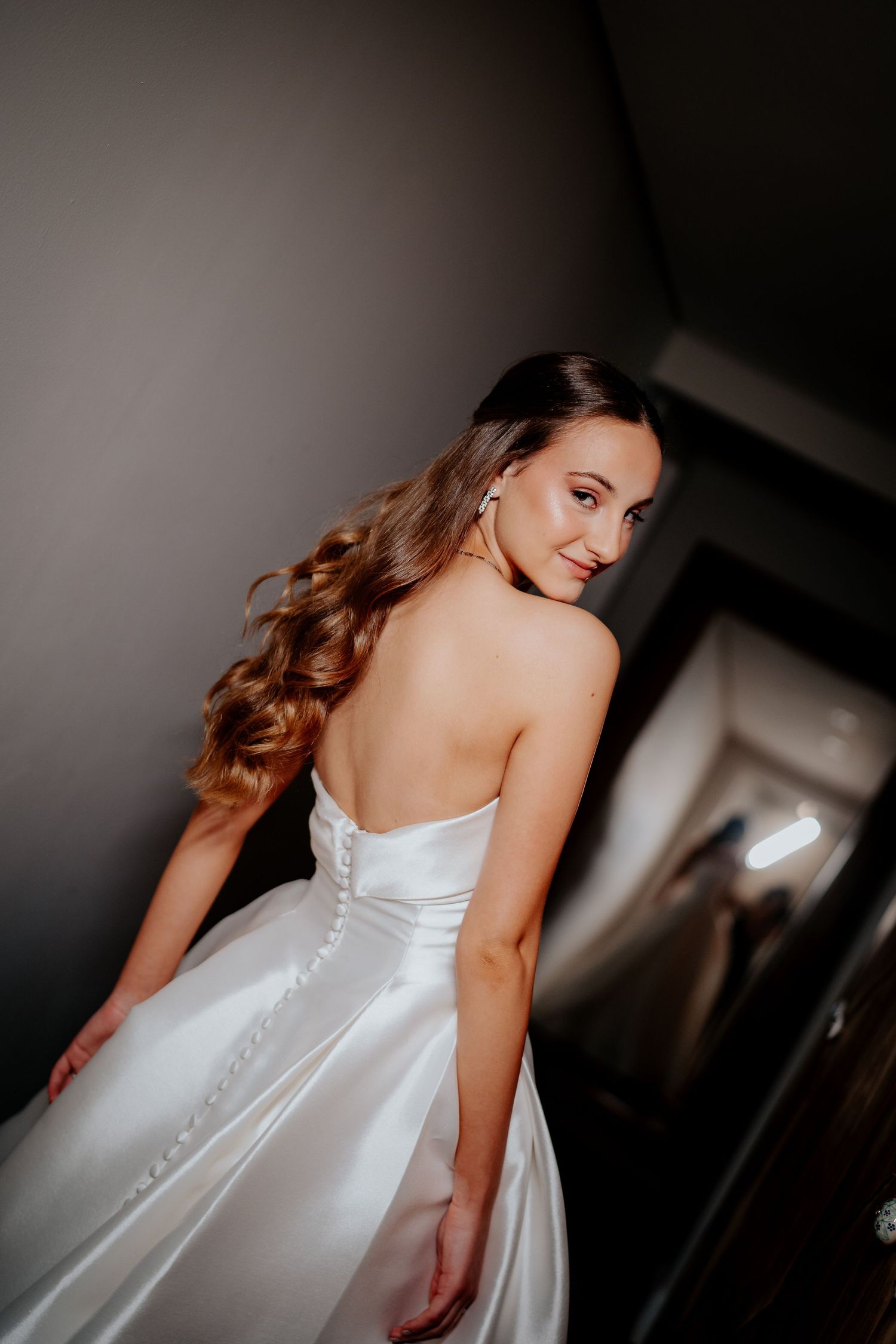 Elegant white wedding gown with corset back photographed in dramatic lighting.