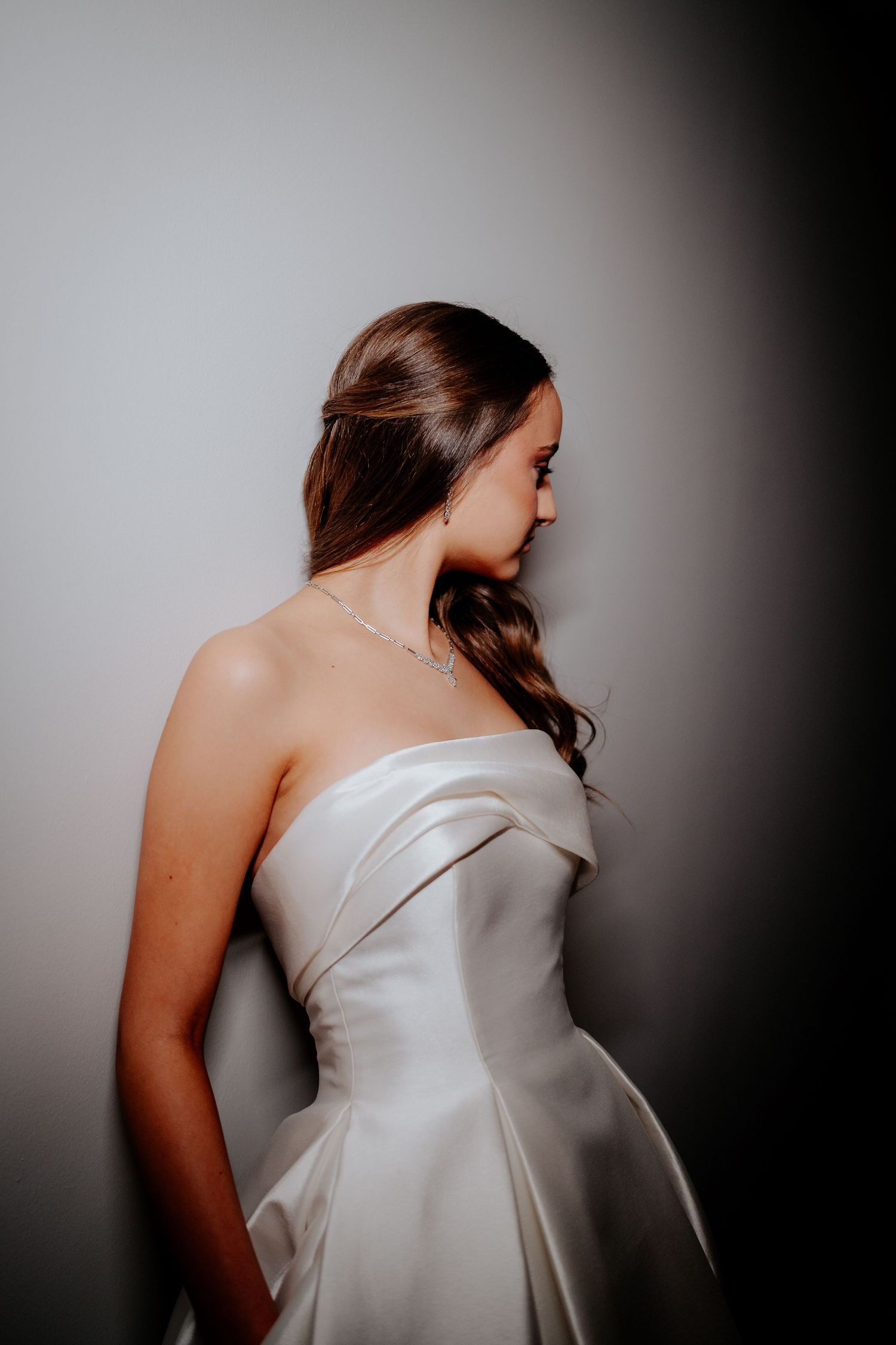 Close-up portrait of figure in elegant white strapless dress against dark background in dramatic lighting.