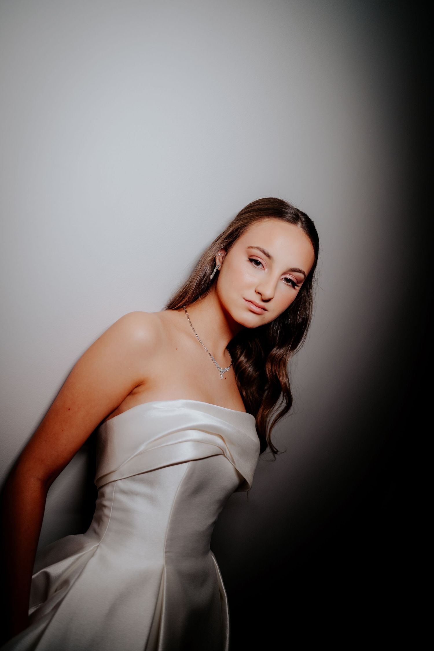 Studio portrait of person in white bridal gown with moody lighting and dark shadows.