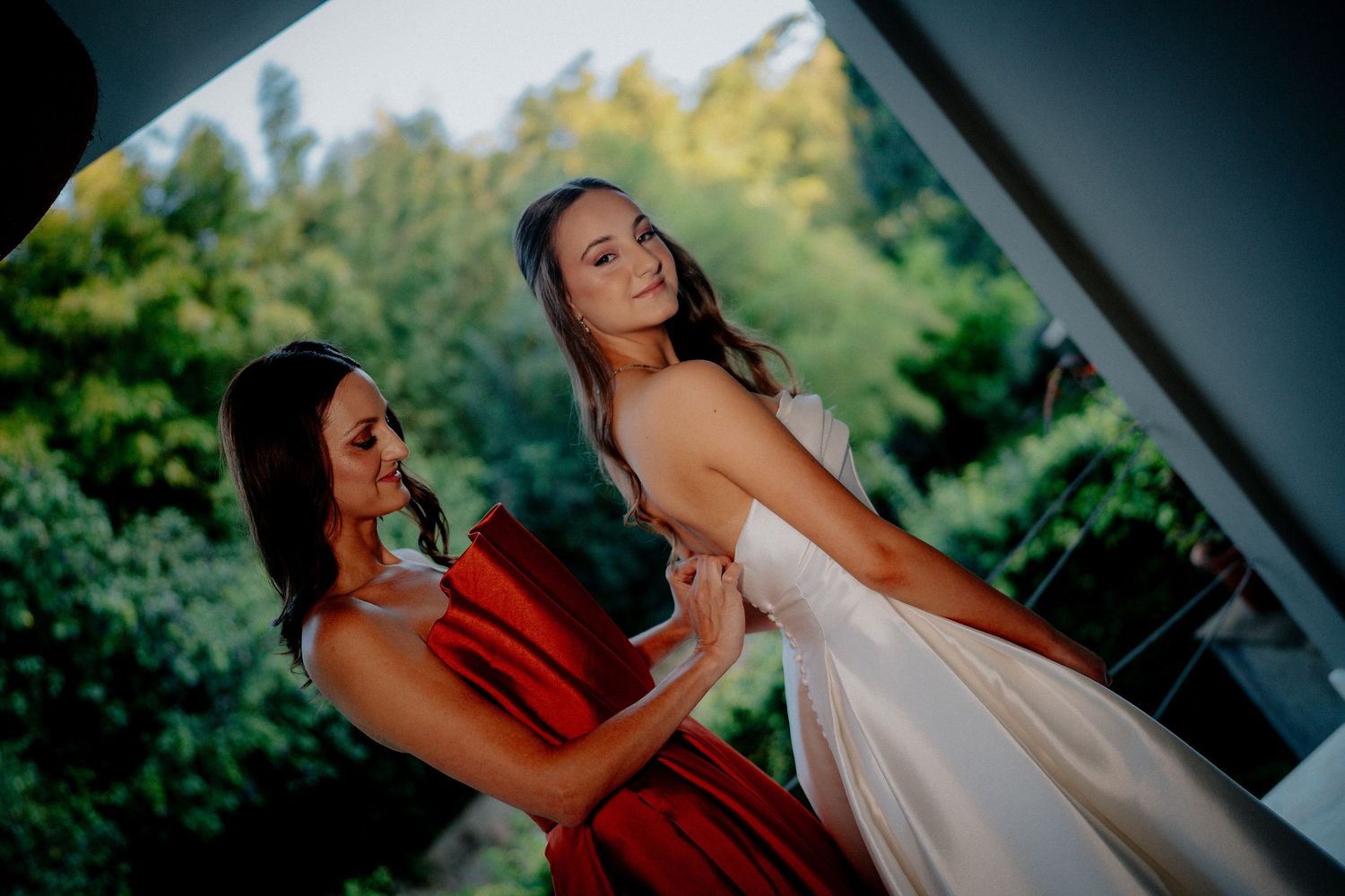 Elegant wedding photography showing figures in white dress and red attire among greenery.