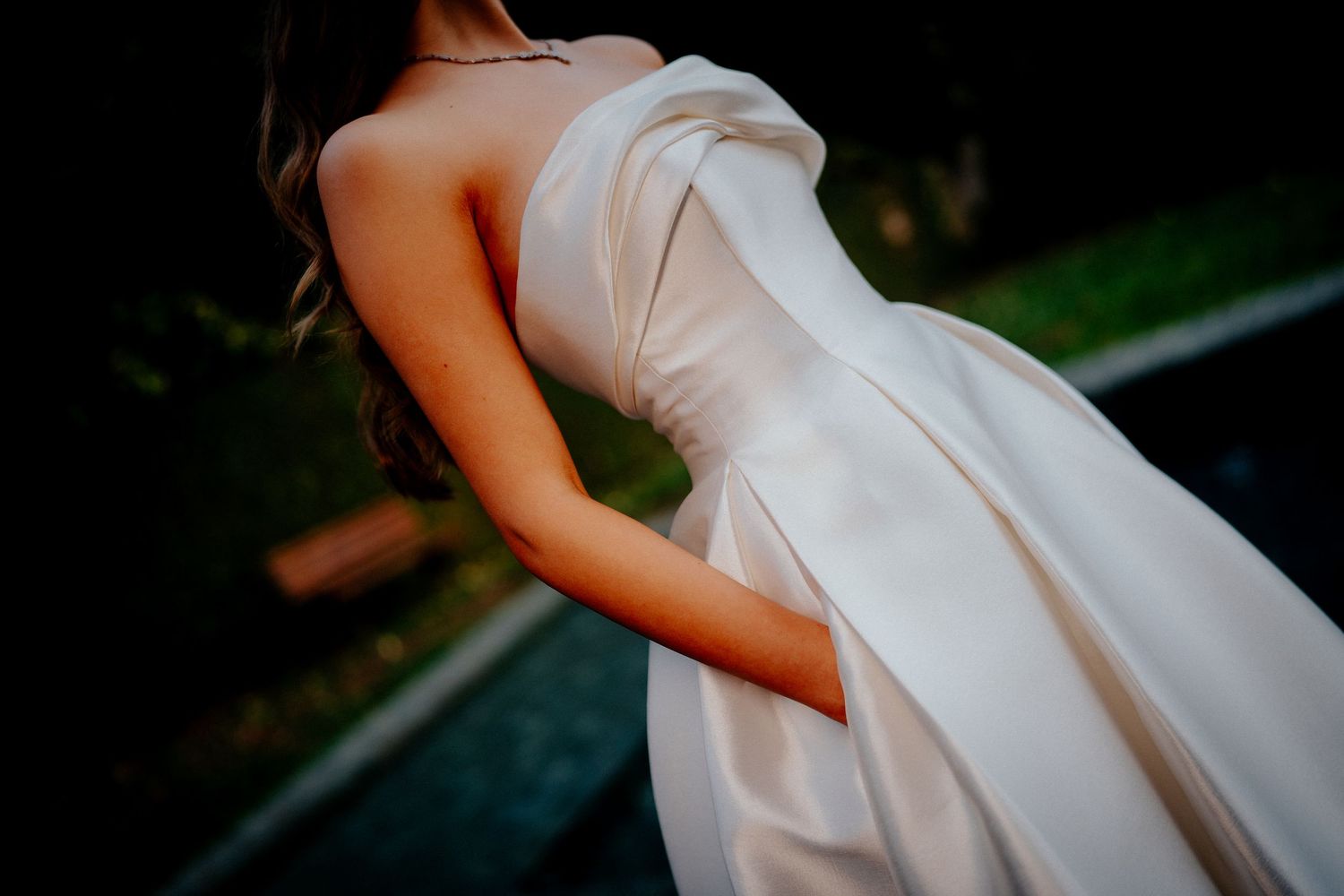 Elegant white bridal gown photographed in natural outdoor setting with dramatic angles.