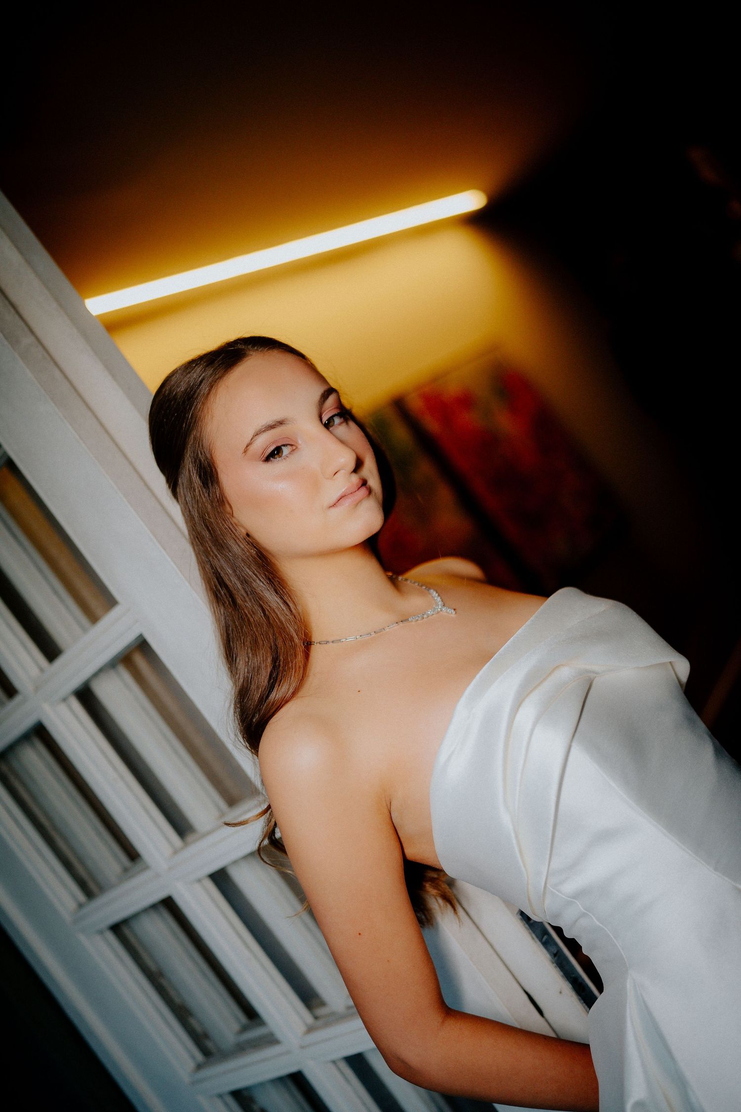 A woman in a white strapless gown poses dramatically in warm lighting.