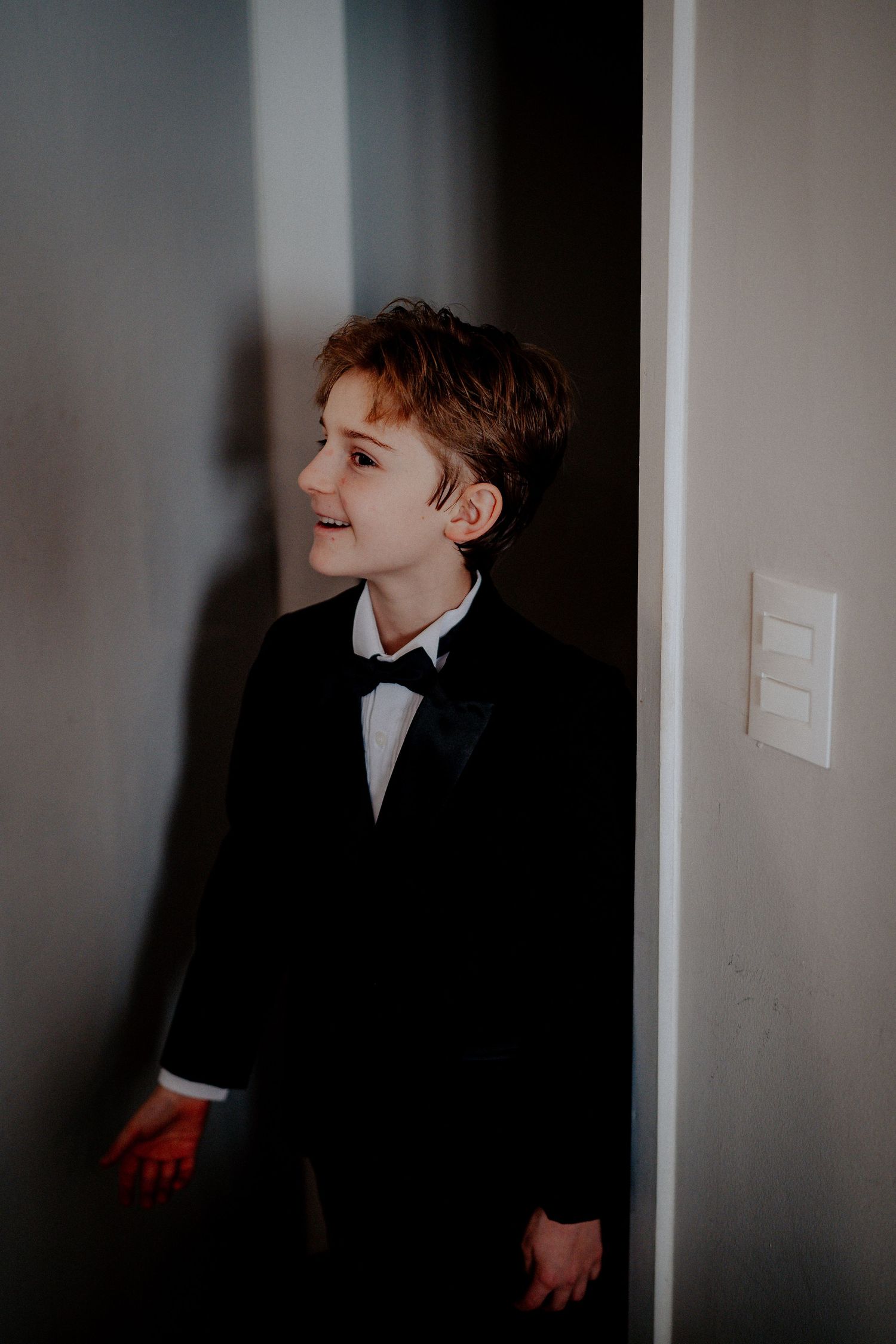 Young attendant in black tuxedo and bowtie stands by doorway.