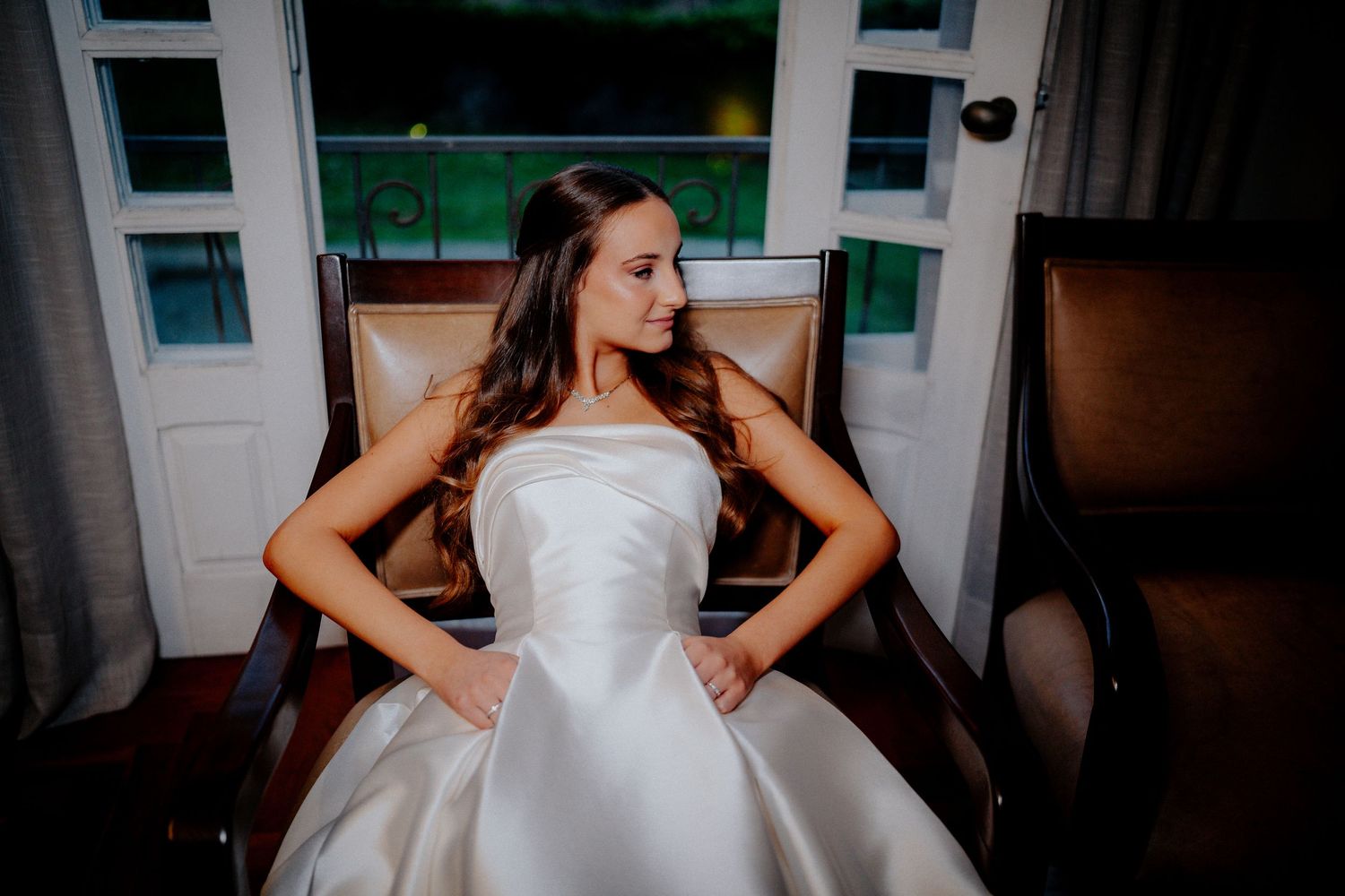 A woman in a classic white wedding gown sits gracefully in a chair.