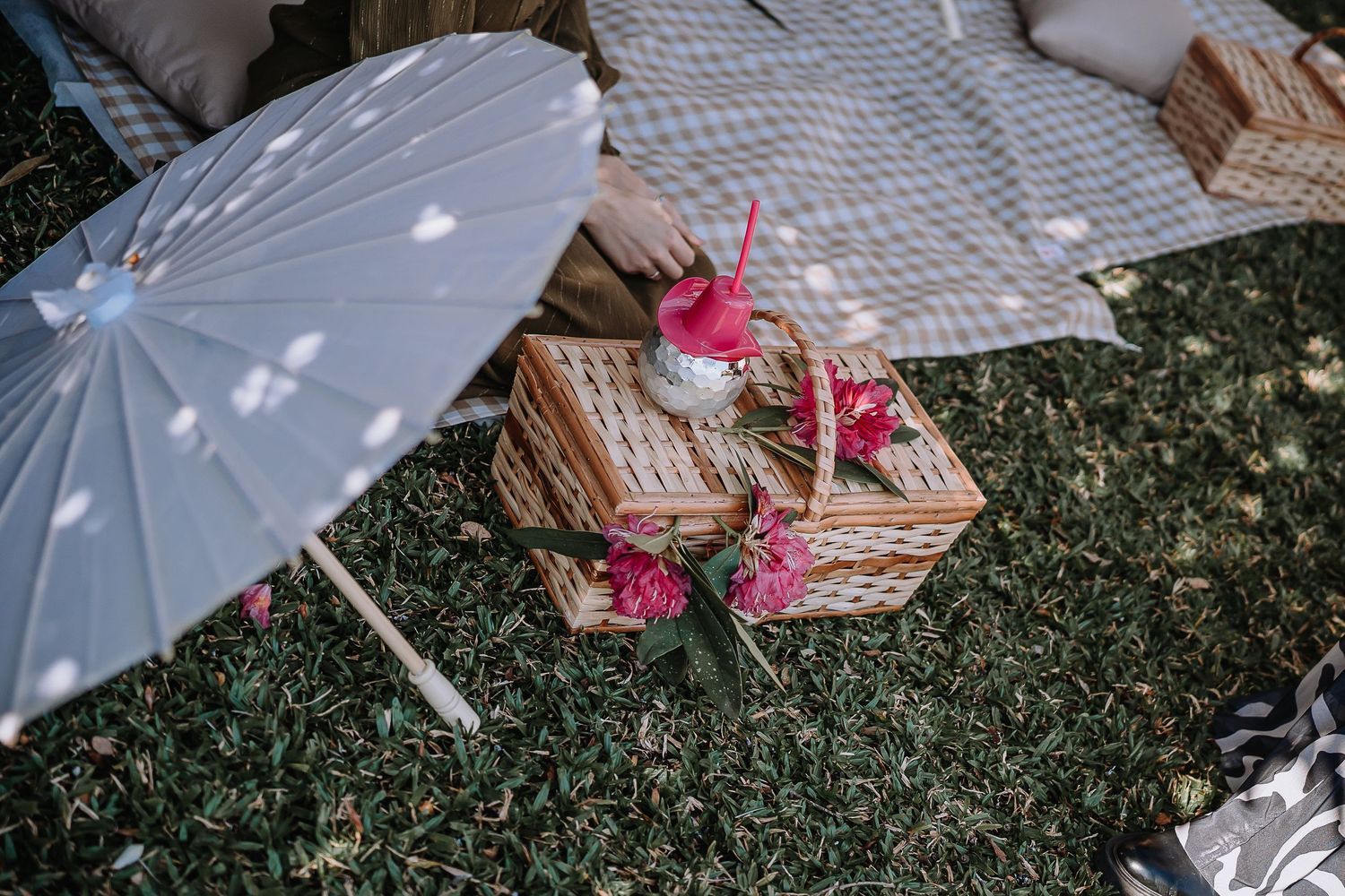 White parasol and pink decorations on picnic blanket in garden setting.