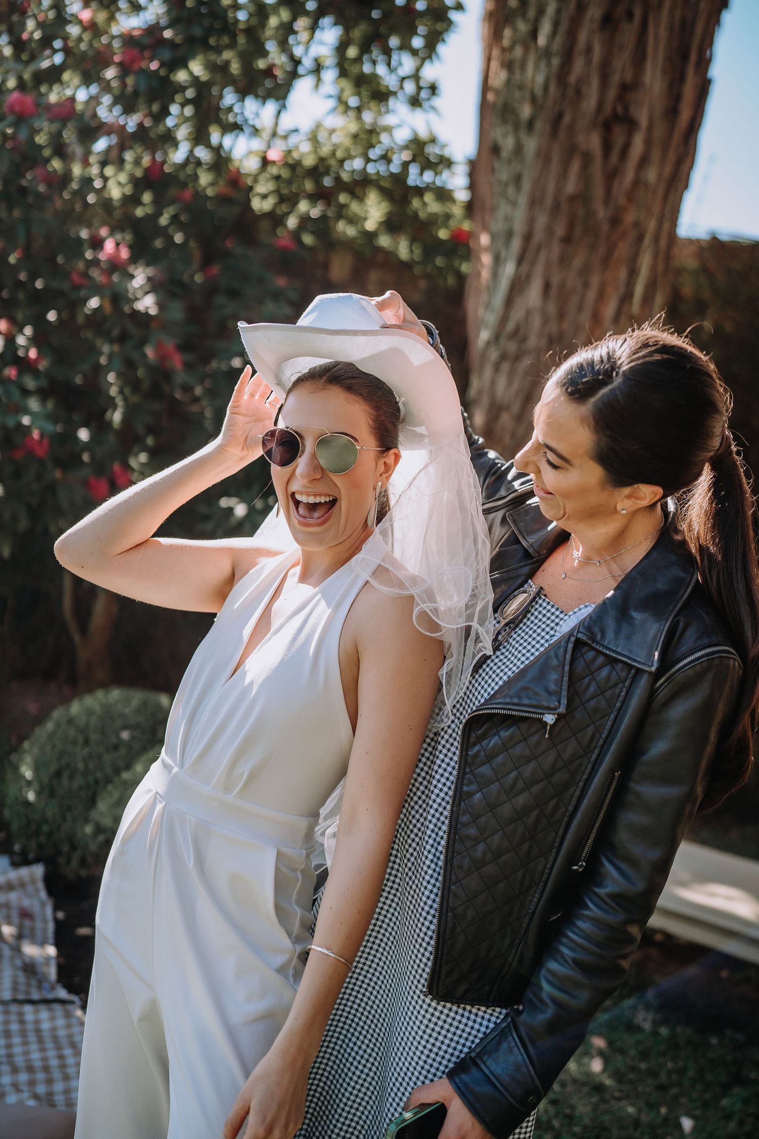 Two people sharing laughter in outdoor setting with trees and flowers in background.