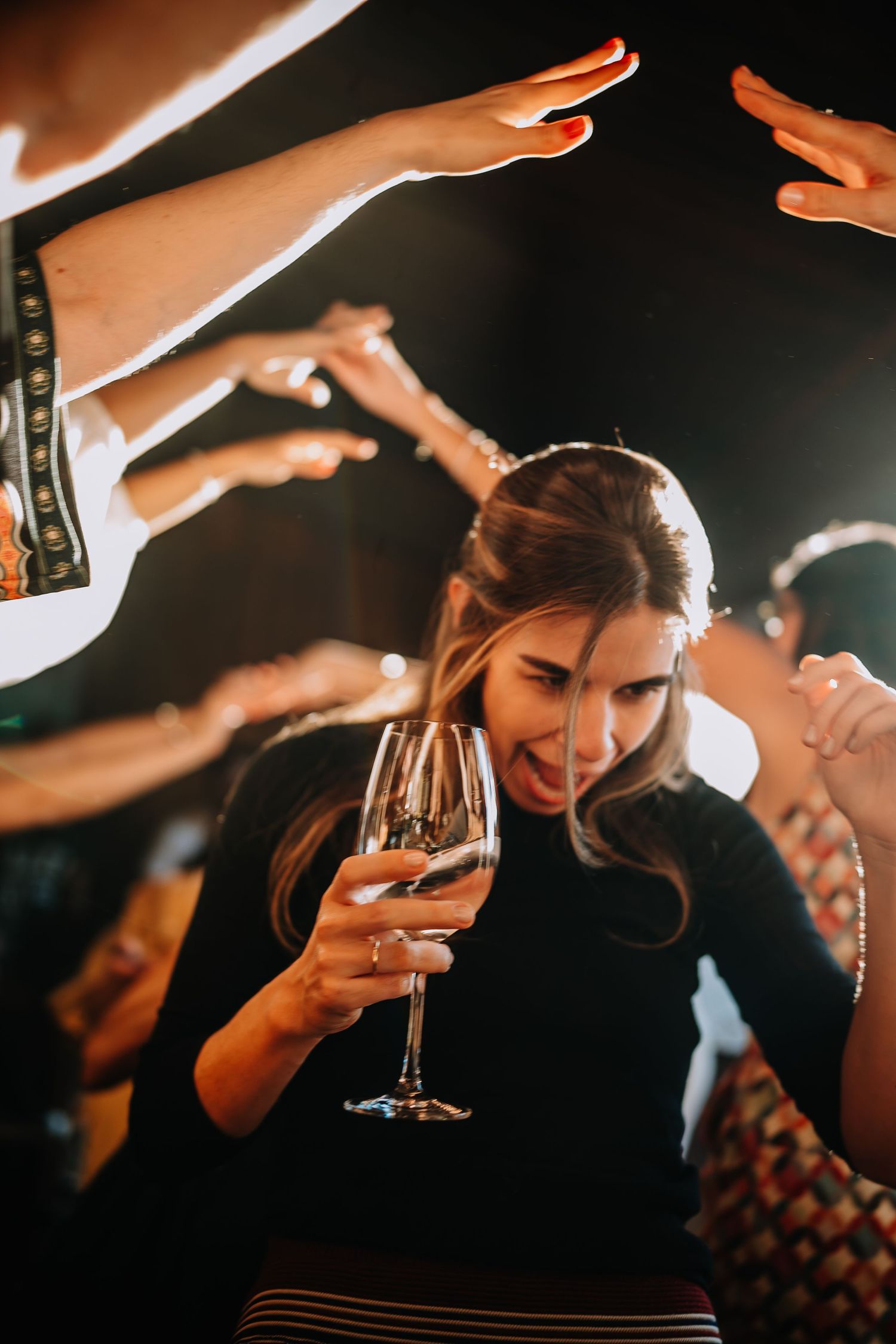 Celebratory moment captured with raised hands and wine glass at evening party.