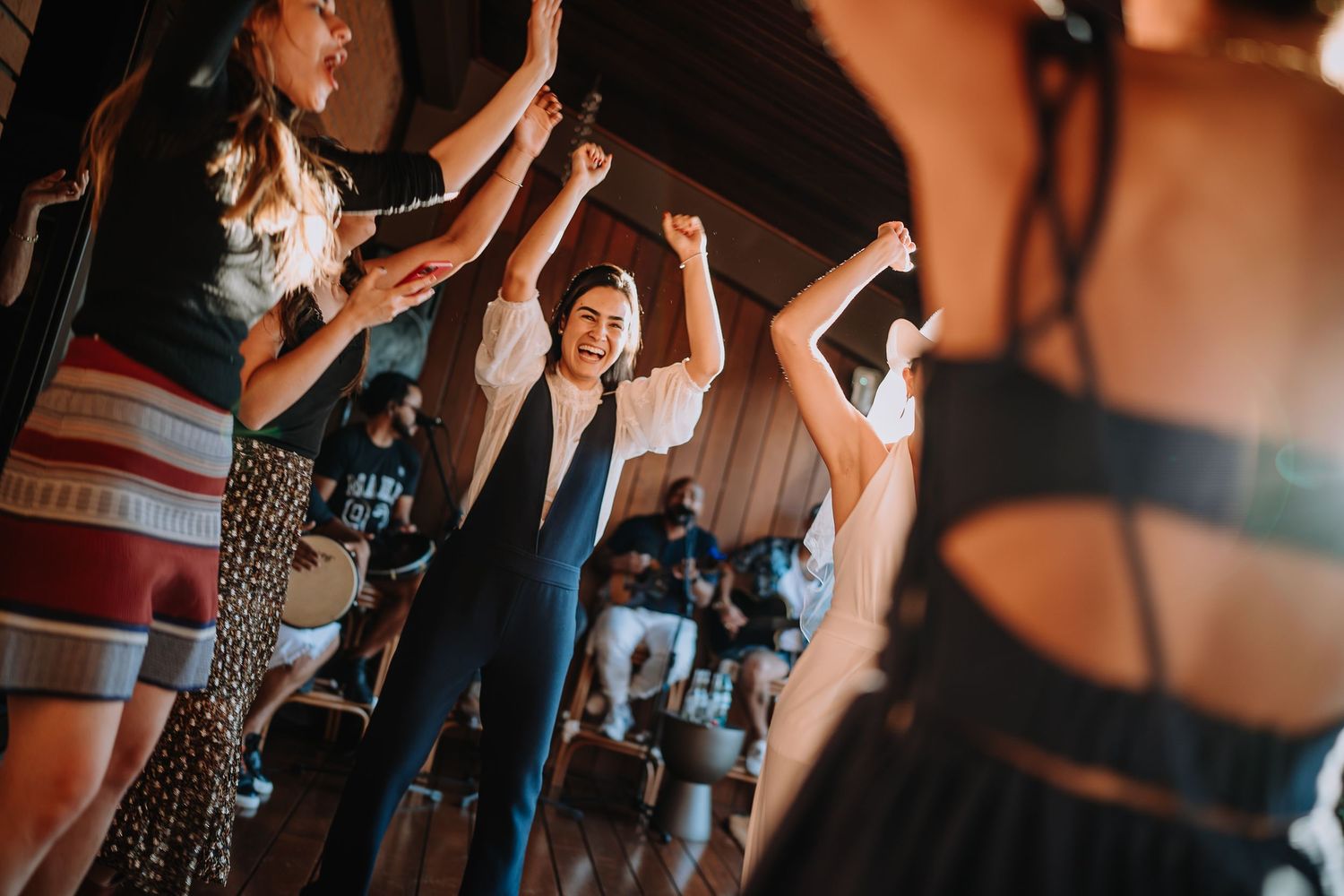 Wedding guests dance and celebrate with raised arms in a dimly lit venue.