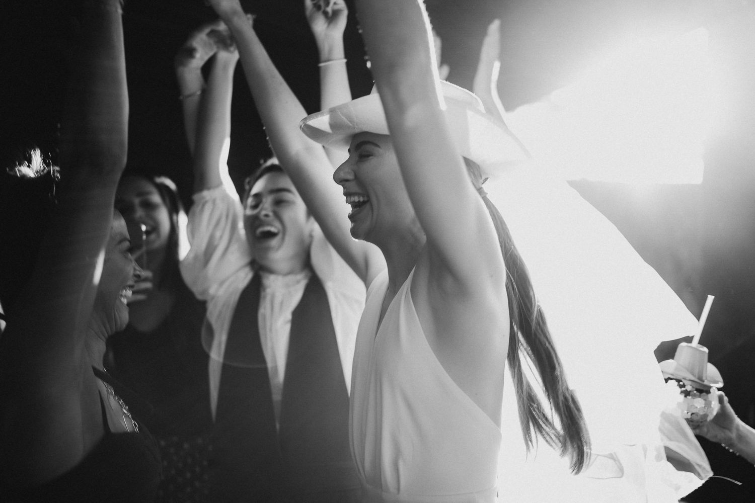 Black and white shot of people dancing with raised arms at a celebration.