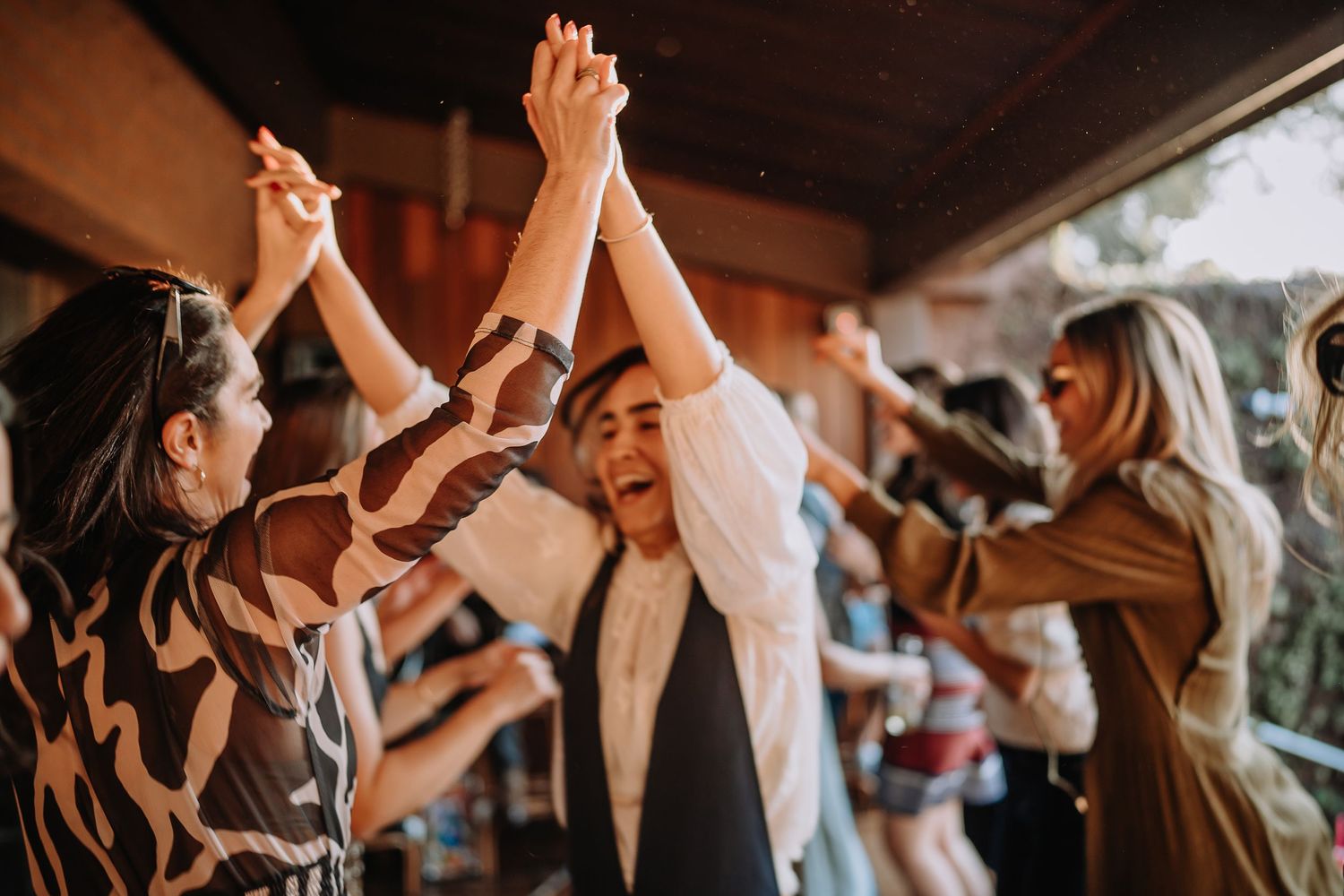 People dance with arms raised at a rustic indoor venue with brick walls.